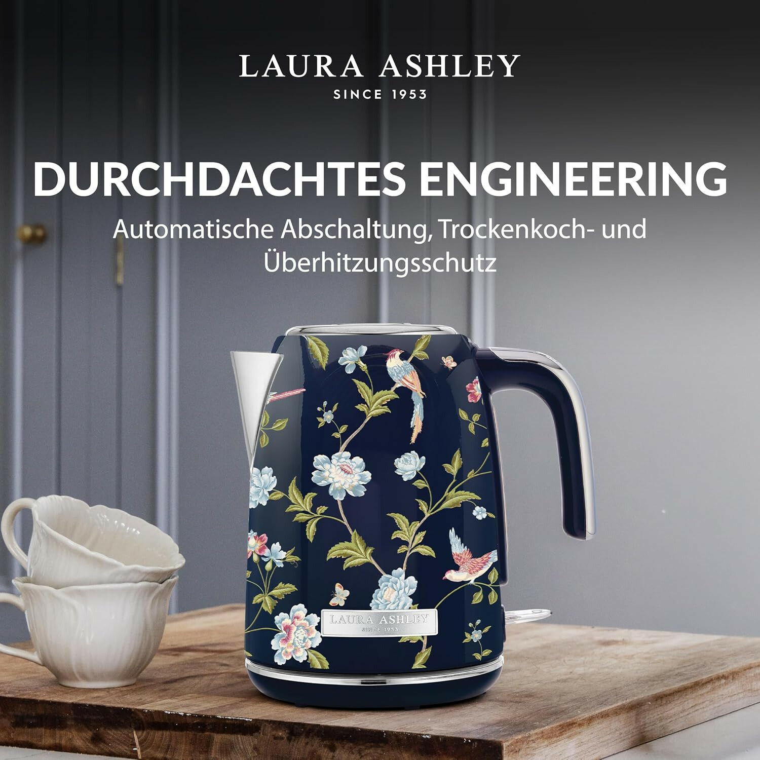 Dunkelblauer Laura Ashley Wasserkocher mit Blumen- und Vogelmuster auf einem Holzbrett.