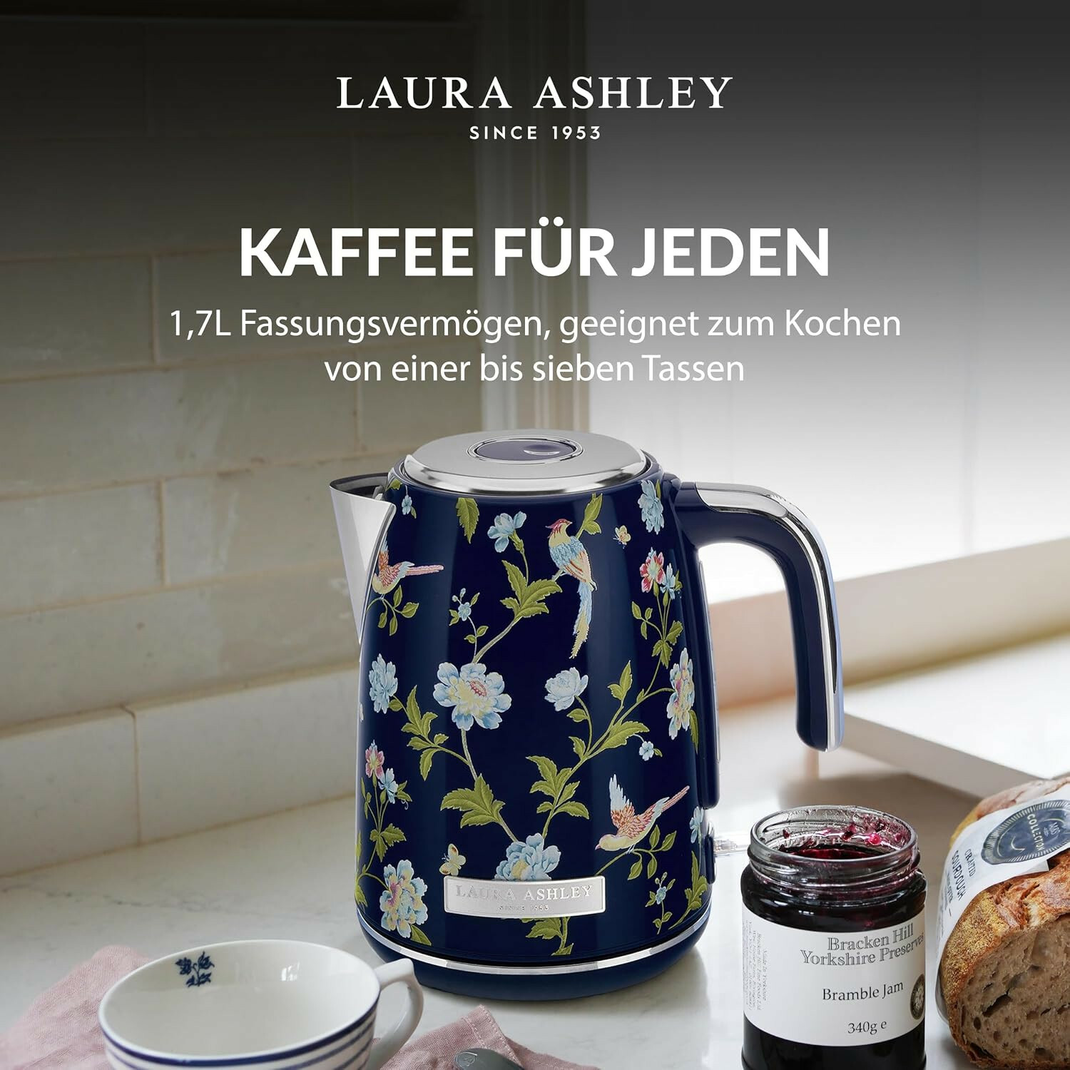 Blauer Laura Ashley Wasserkocher mit Blumenmuster, daneben Marmeladenglas, Brot und Tasse in einer Küche.