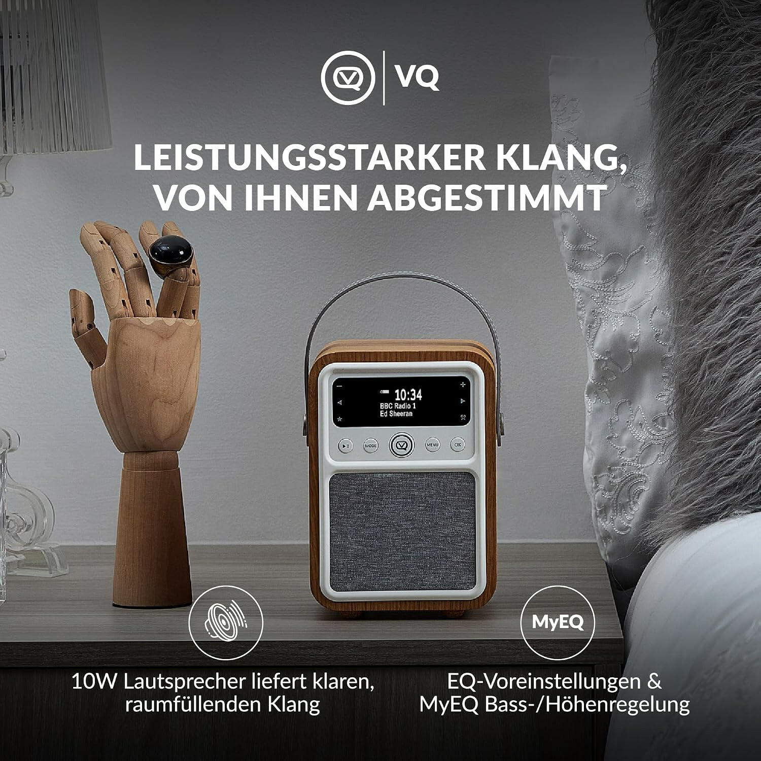 Ein Holzradio mit Stofffront steht auf einem Nachttisch neben einer hölzernen Hand und einem Bett.