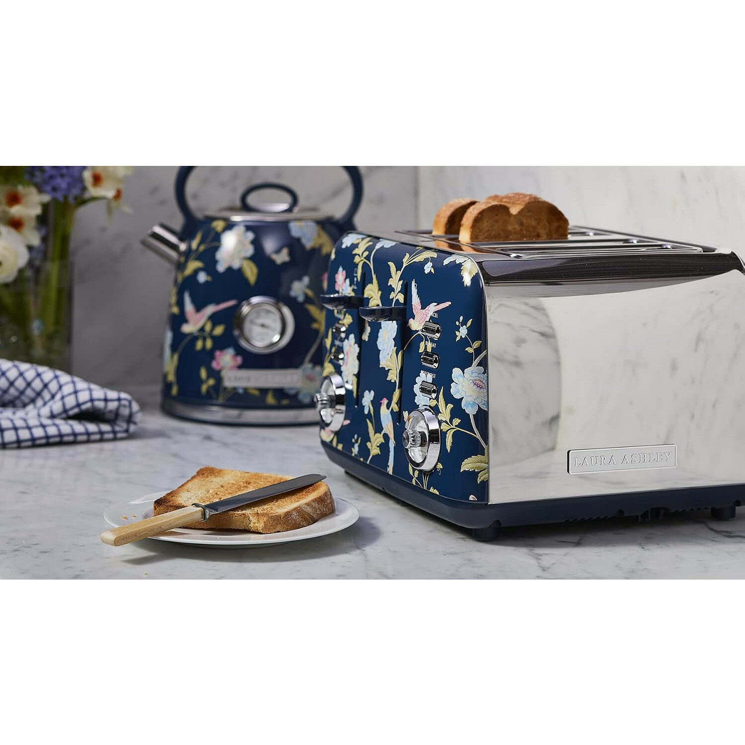Ein blauer Toaster und Wasserkocher mit Blumenmuster stehen auf einer Marmorarbeitsplatte, davor Toast.