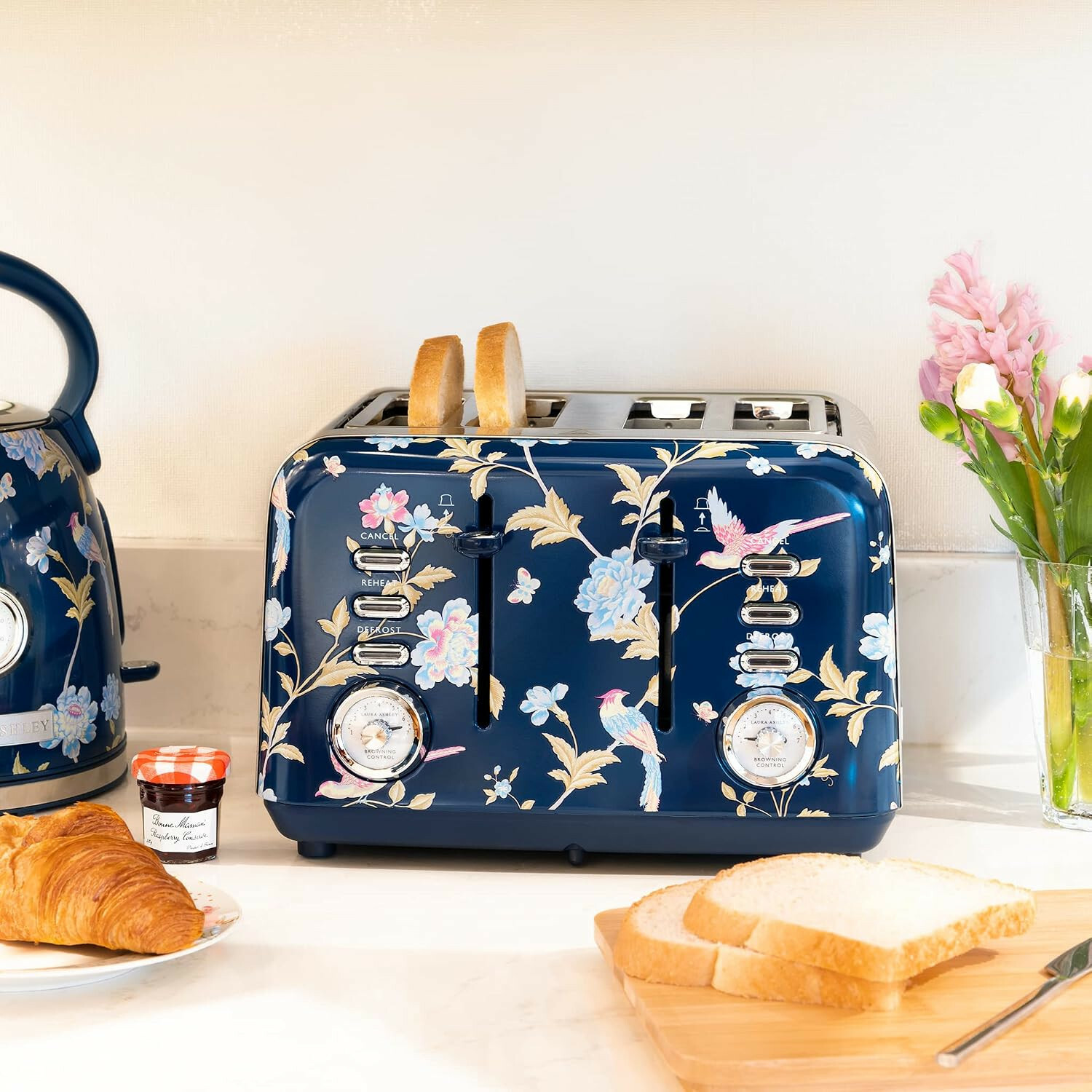 Ein blauer Toaster mit Blumenmuster, Brot, Croissants, Marmelade und Blumen auf einer Küchenzeile.