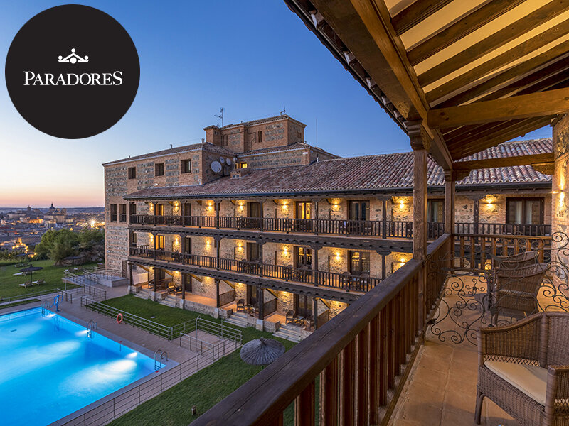 Hotel de piedra iluminado con balcones, piscina y jardín al atardecer.