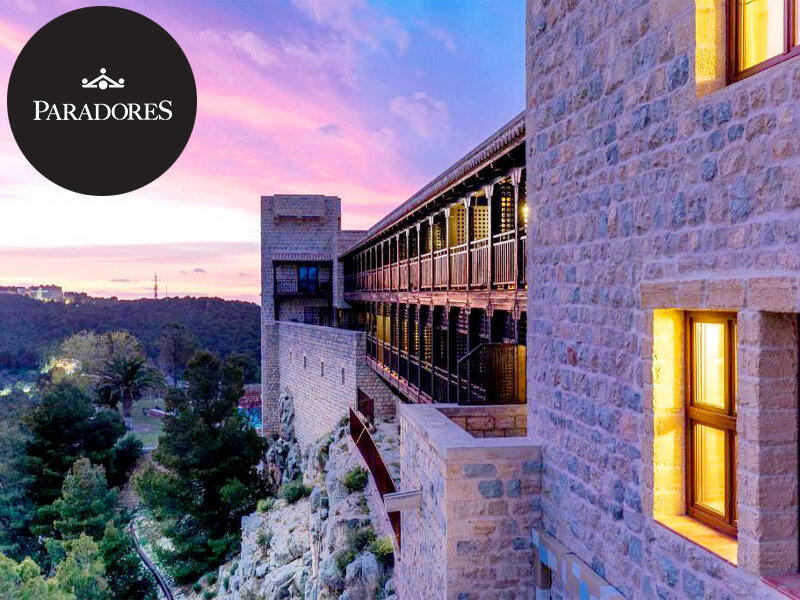 Edificio de piedra con balcón de madera en ladera rocosa al atardecer.