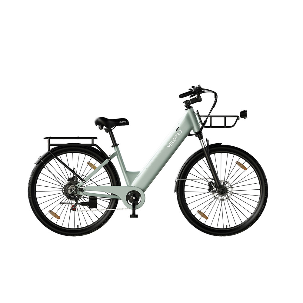 Una bicicleta eléctrica de ciudad verde claro con sillín negro, cesta delantera y parrilla trasera sobre fondo blanco.