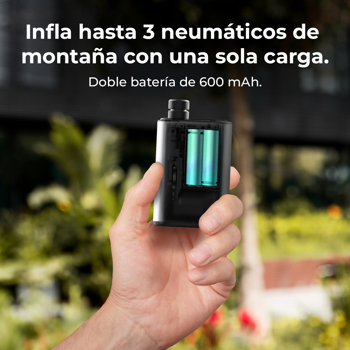 Una mano sostiene un mini dispositivo negro con baterías visibles, sobre un fondo natural borroso.