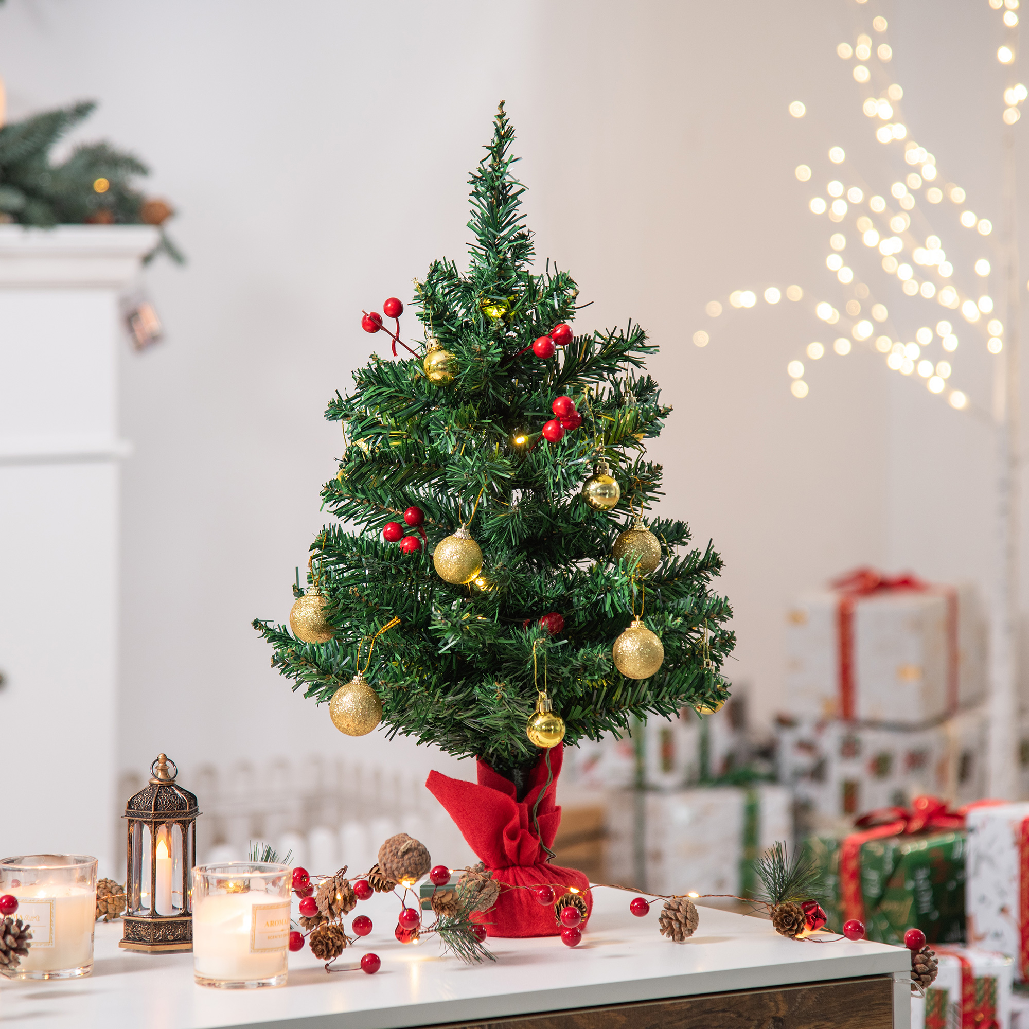Pequeño árbol de Navidad decorado con adornos dorados, bayas rojas y luces en una mesa.