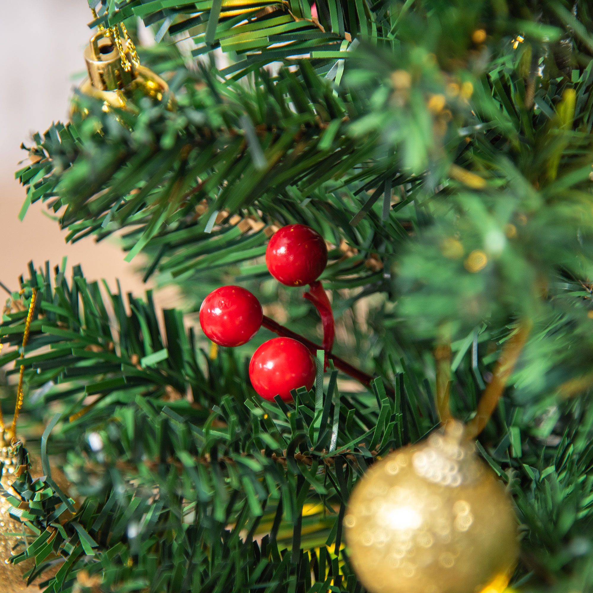 Tres bayas rojas en un árbol de Navidad verde con adornos dorados.