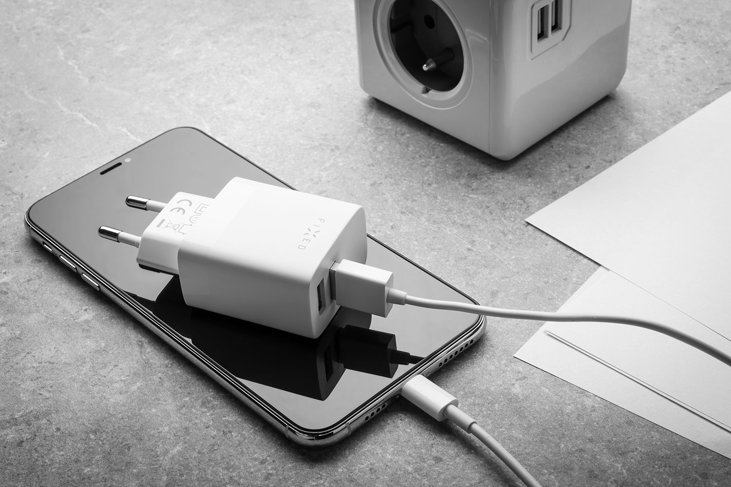 Ein Smartphone und ein weißes Ladegerät mit Kabel liegen auf einem Tisch neben einem Steckdosenwürfel.