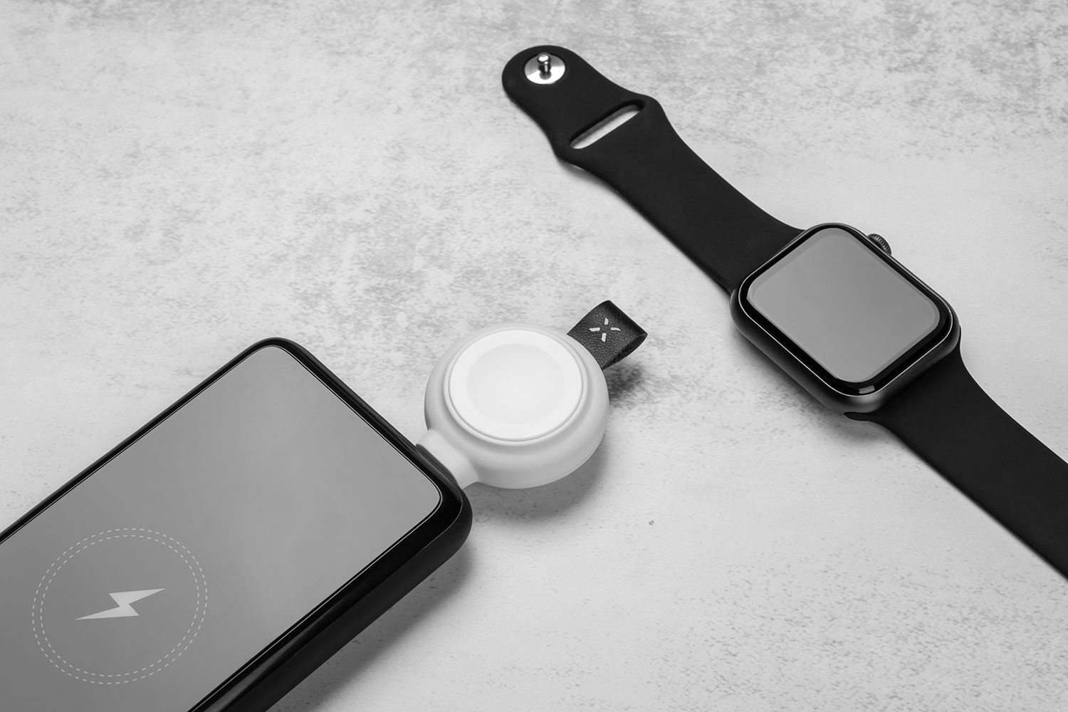 Ein Smartphone und eine Smartwatch auf einer grauen Oberfläche mit einem runden Lade-Accessoire.