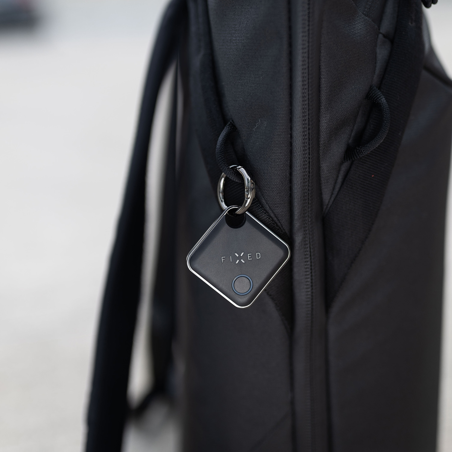 Ein schwarzer GPS-Tracker mit der Aufschrift FIXED hängt an einem schwarzen Rucksack.