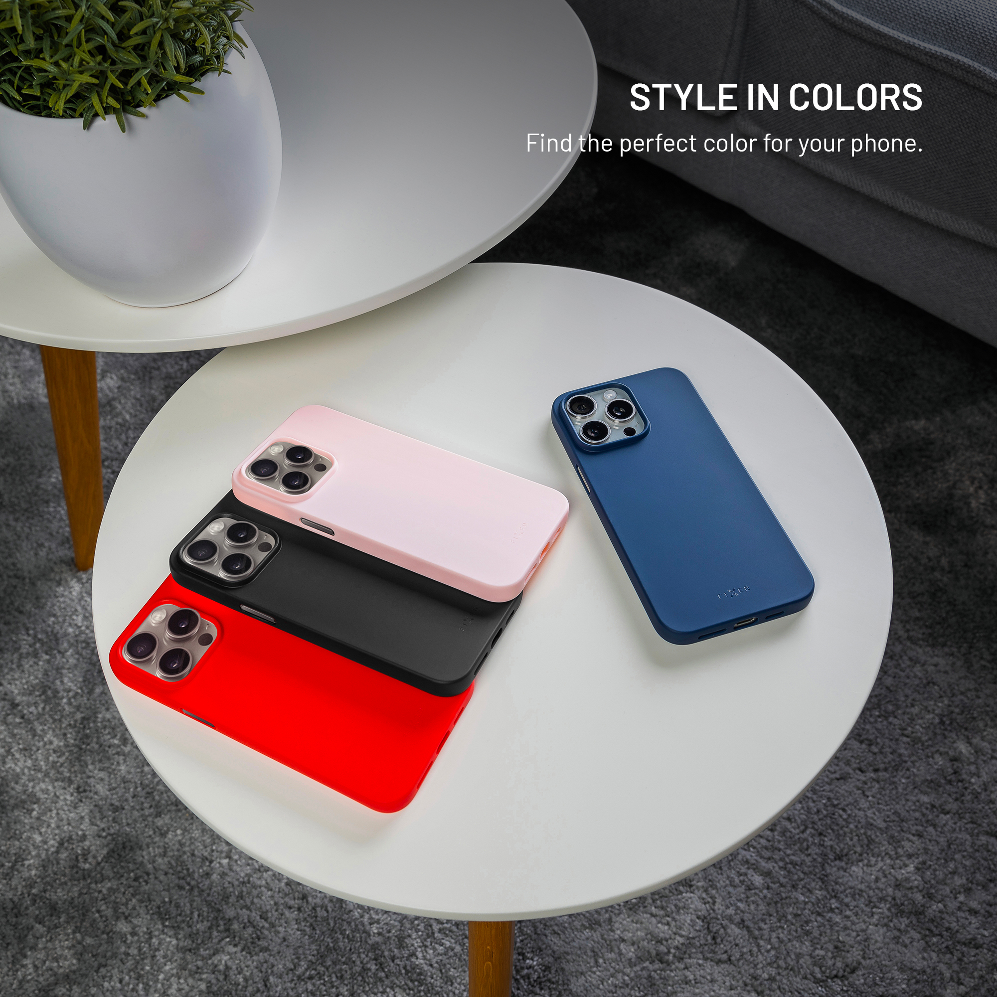 Vier Smartphones in roten, schwarzen, rosa und blauen Hüllen liegen neben einer Pflanze und einem grauen Sofa.