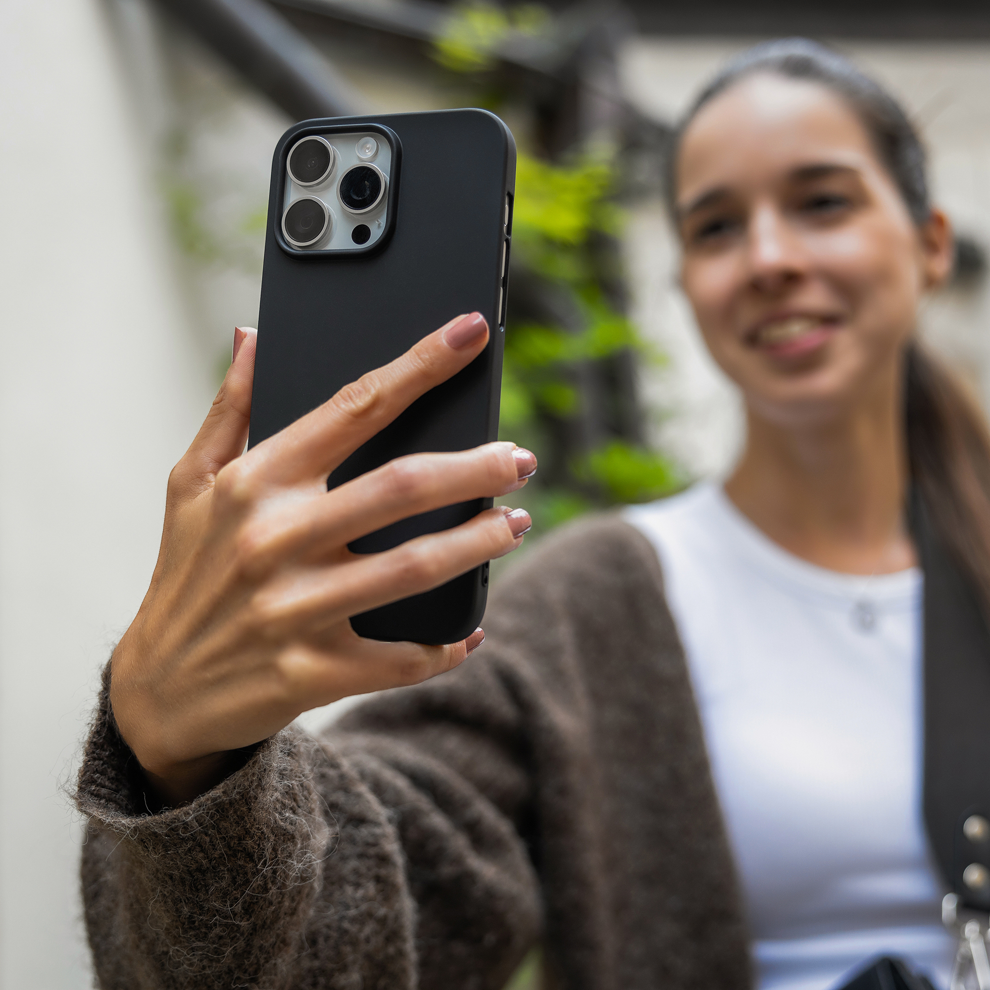 Eine Frau hält ein Smartphone mit schwarzer Hülle in der Hand und macht ein Foto vor grünem Hintergrund.