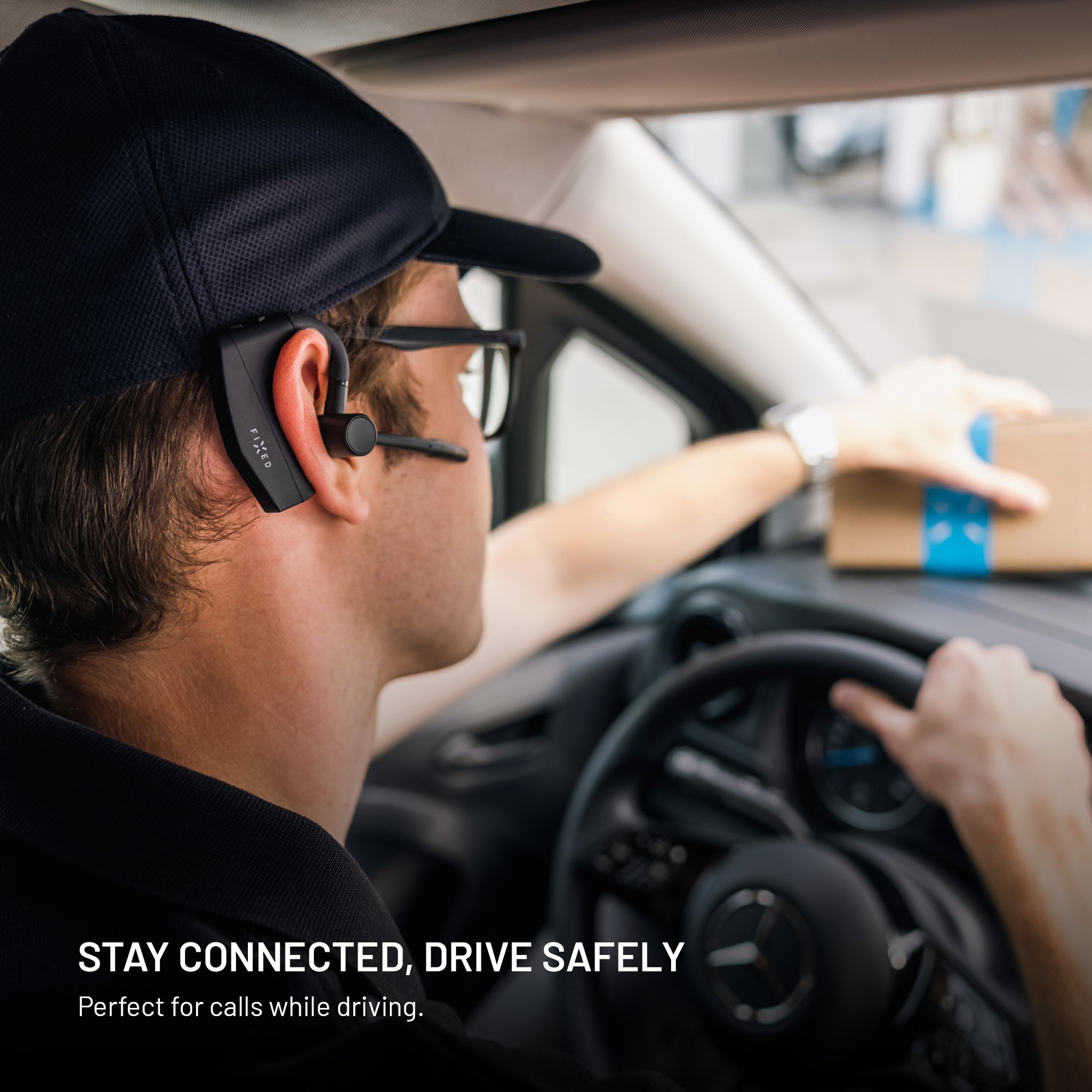 Ein Fahrer mit Kappe und Bluetooth-Headset sitzt am Lenkrad eines Autos und greift nach einem Paket.
