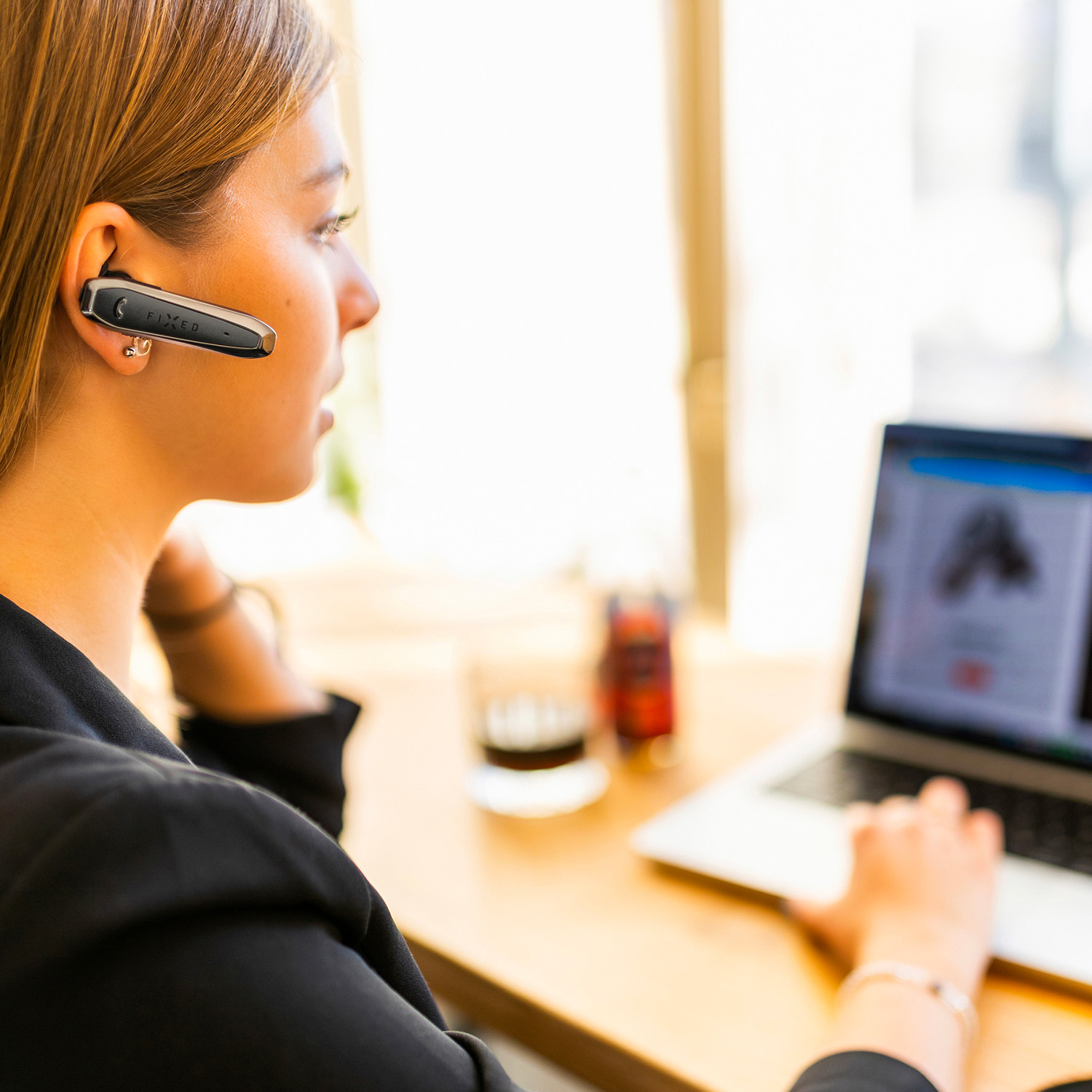 Frau mit Headset arbeitet am Laptop in einem hellen Raum.