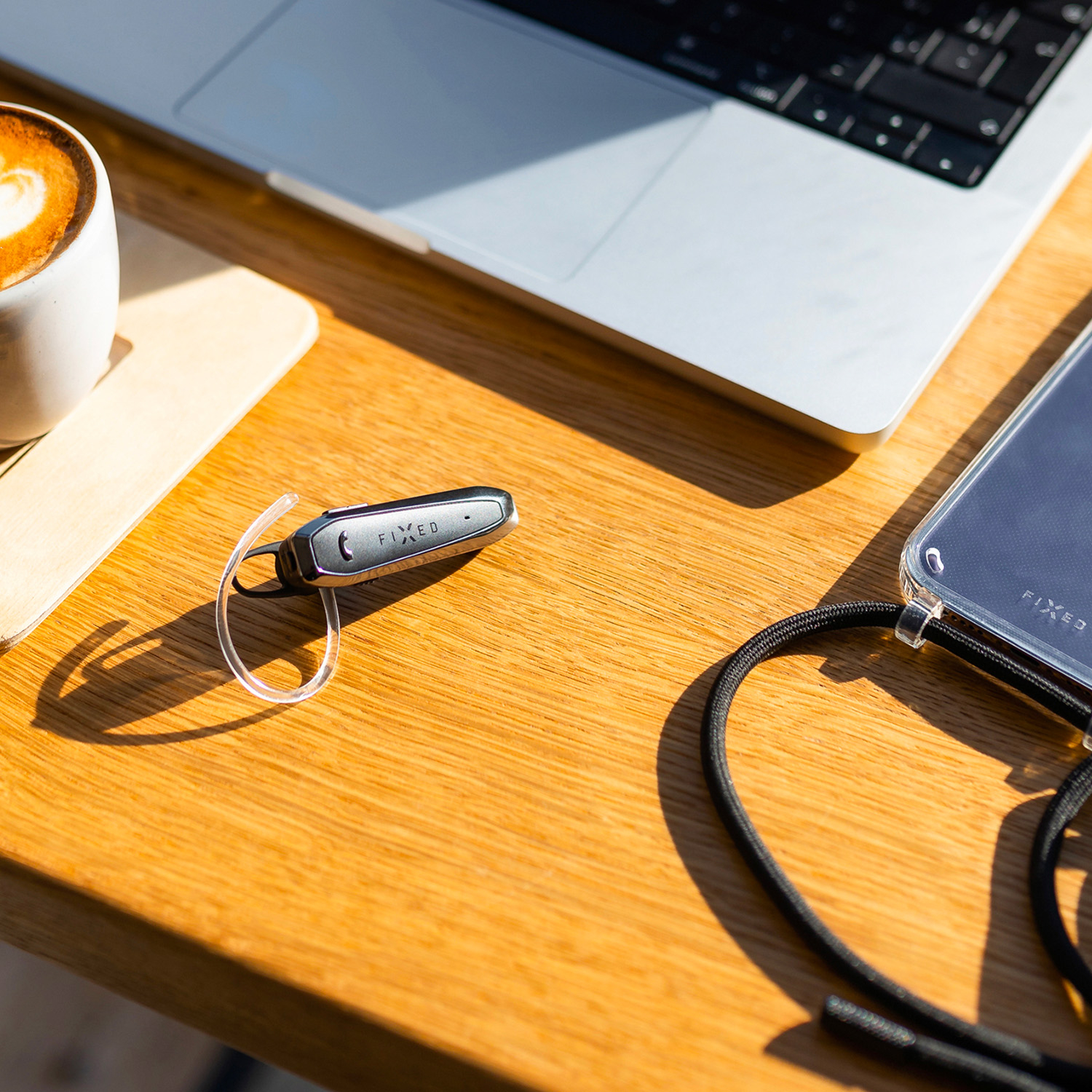 Ein schwarzes Bluetooth-Headset auf einem Holztisch, neben Laptop, Kaffeetasse und Smartphone.