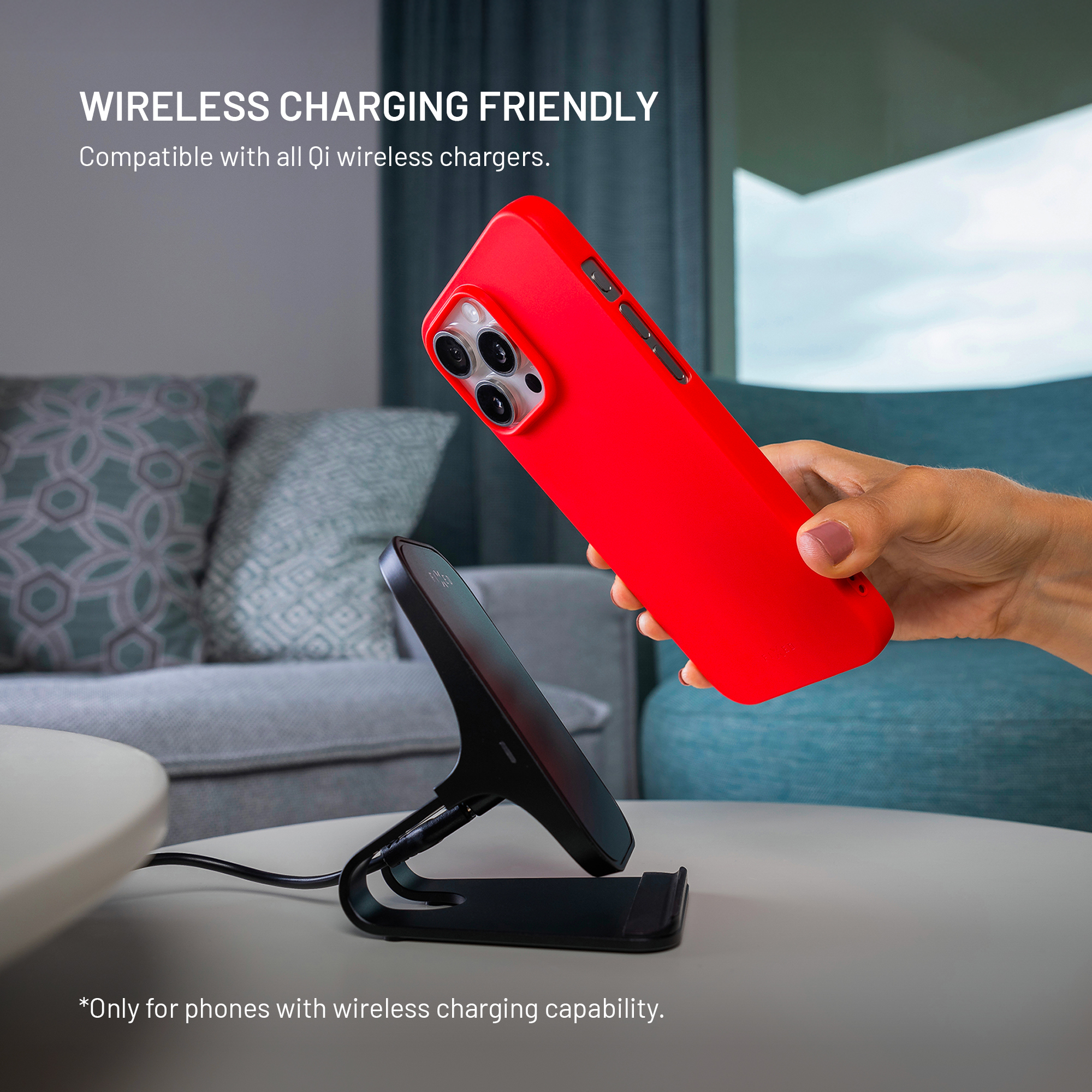 Eine Hand hält ein rotes Smartphone über eine schwarze kabellose Ladestation auf einem Tisch.