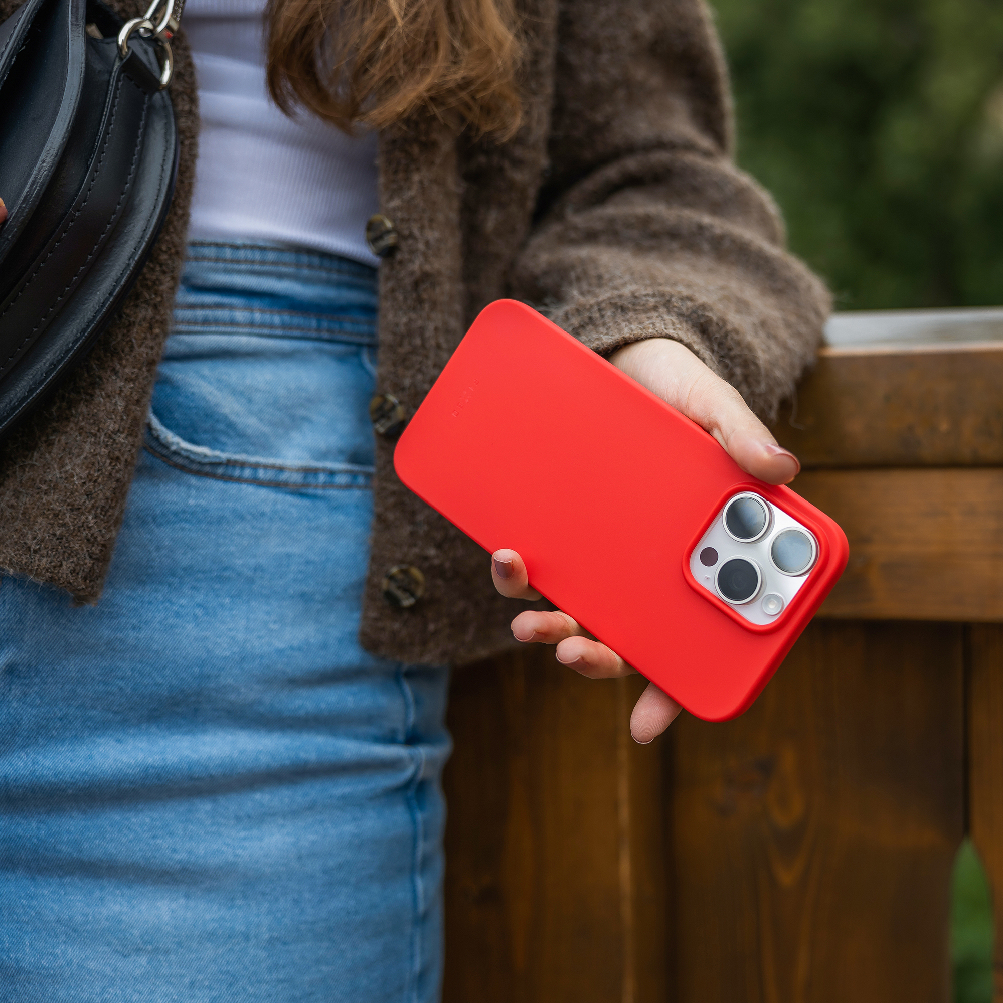 Eine Frau im braunen Cardigan hält ein leuchtend rotes Smartphone mit dreifacher Kamera in der Hand.