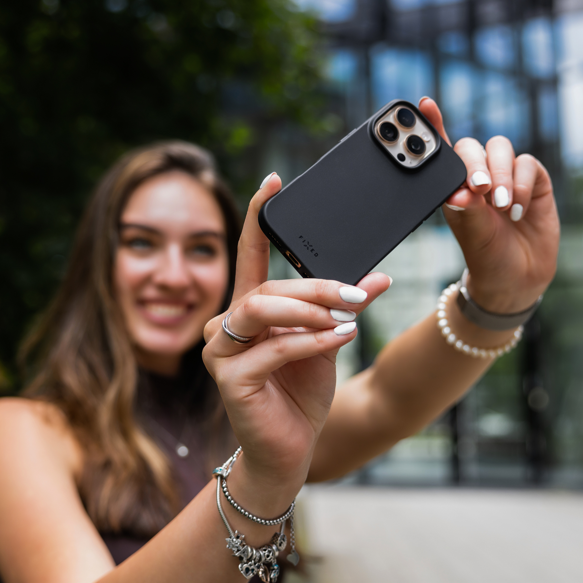 Eine Frau hält ein schwarzes Smartphone und macht im Freien ein Selfie.