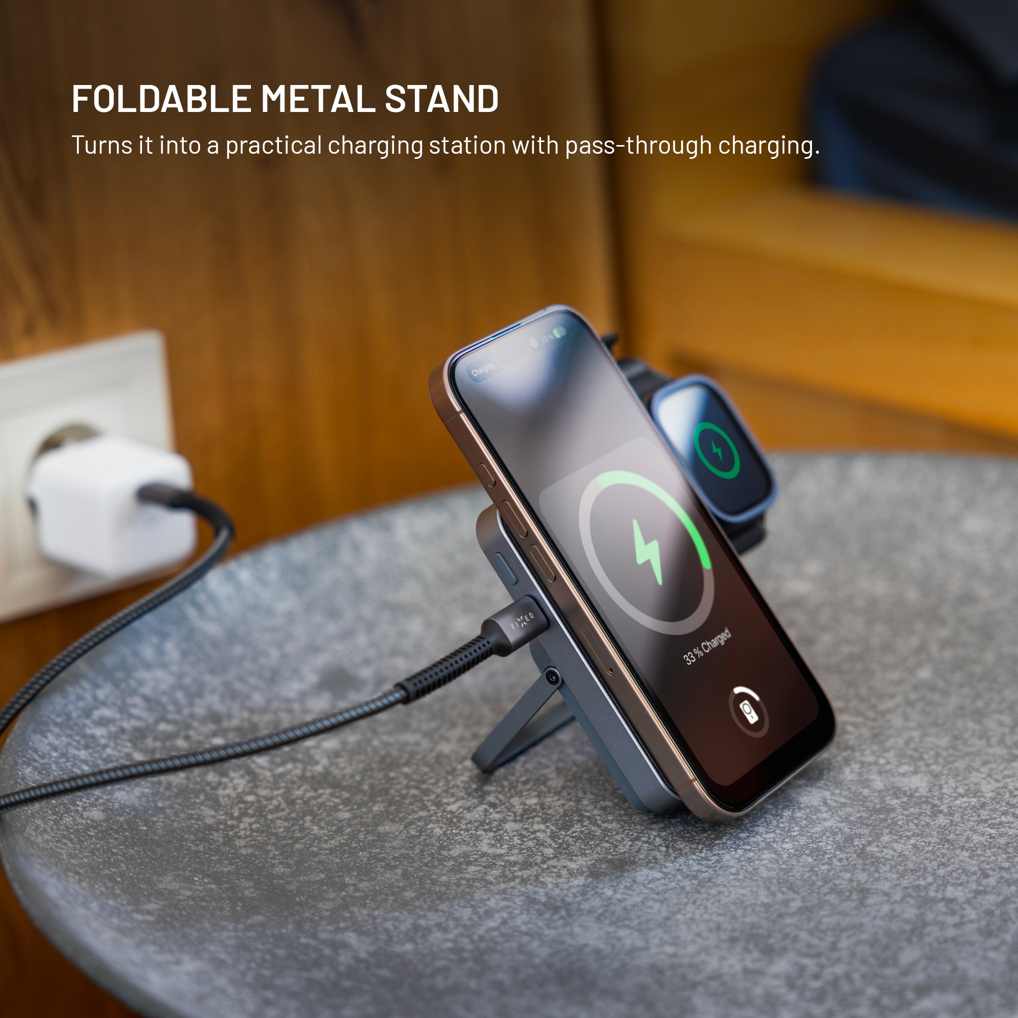 Un supporto in metallo pieghevole carica uno smartphone e uno smartwatch collegati a una presa.