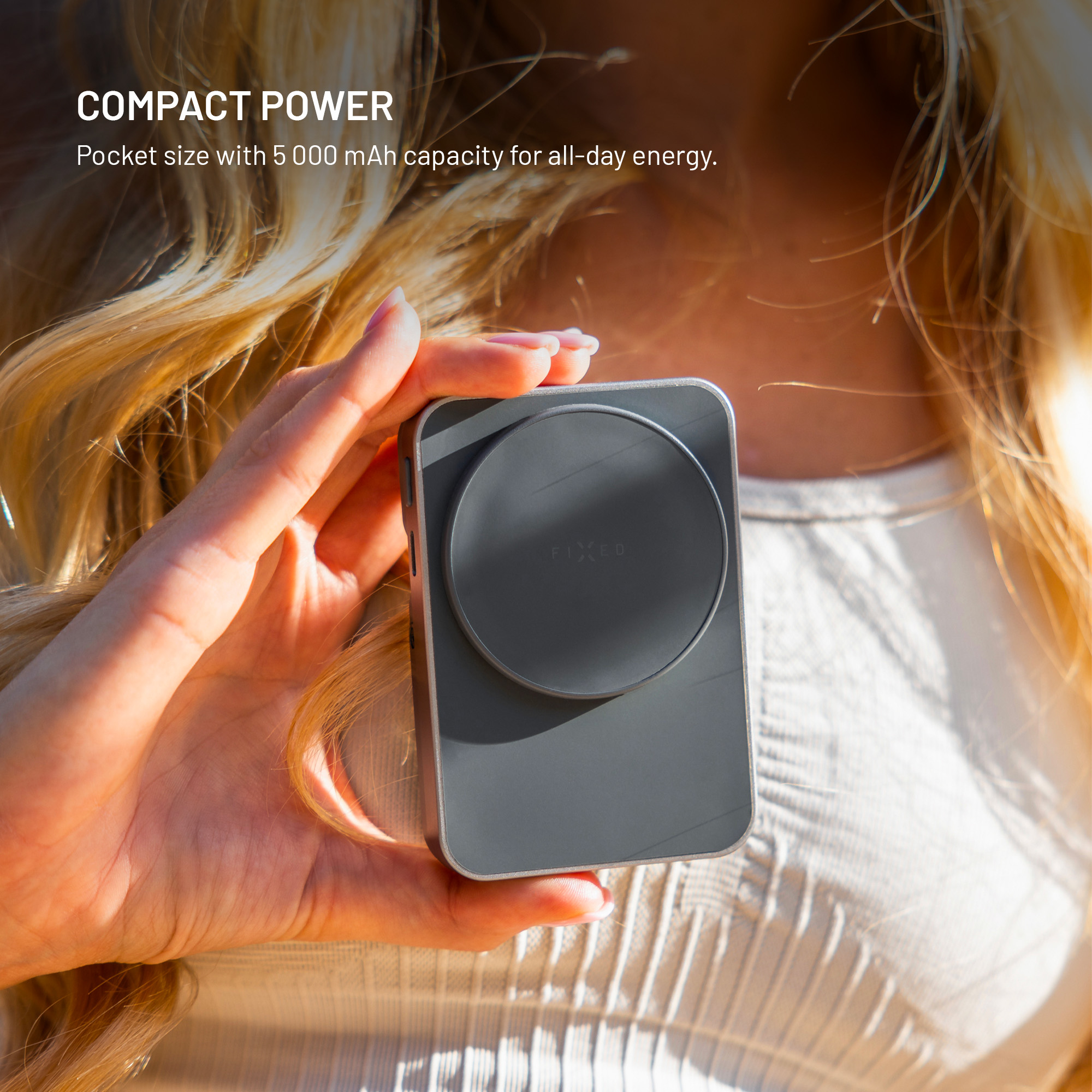 Una donna tiene in mano un power bank grigio compatto con un pad magnetico.