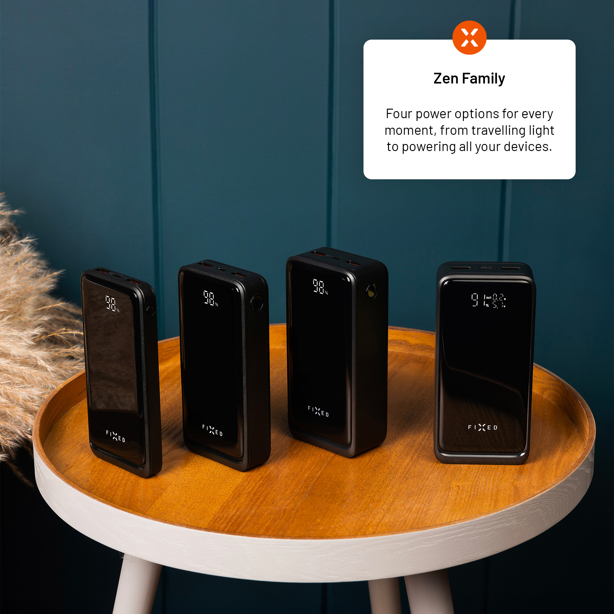 Vier schwarze Powerbanks der Zen-Familie stehen nebeneinander auf einem Holztisch vor einer dunklen Wand.