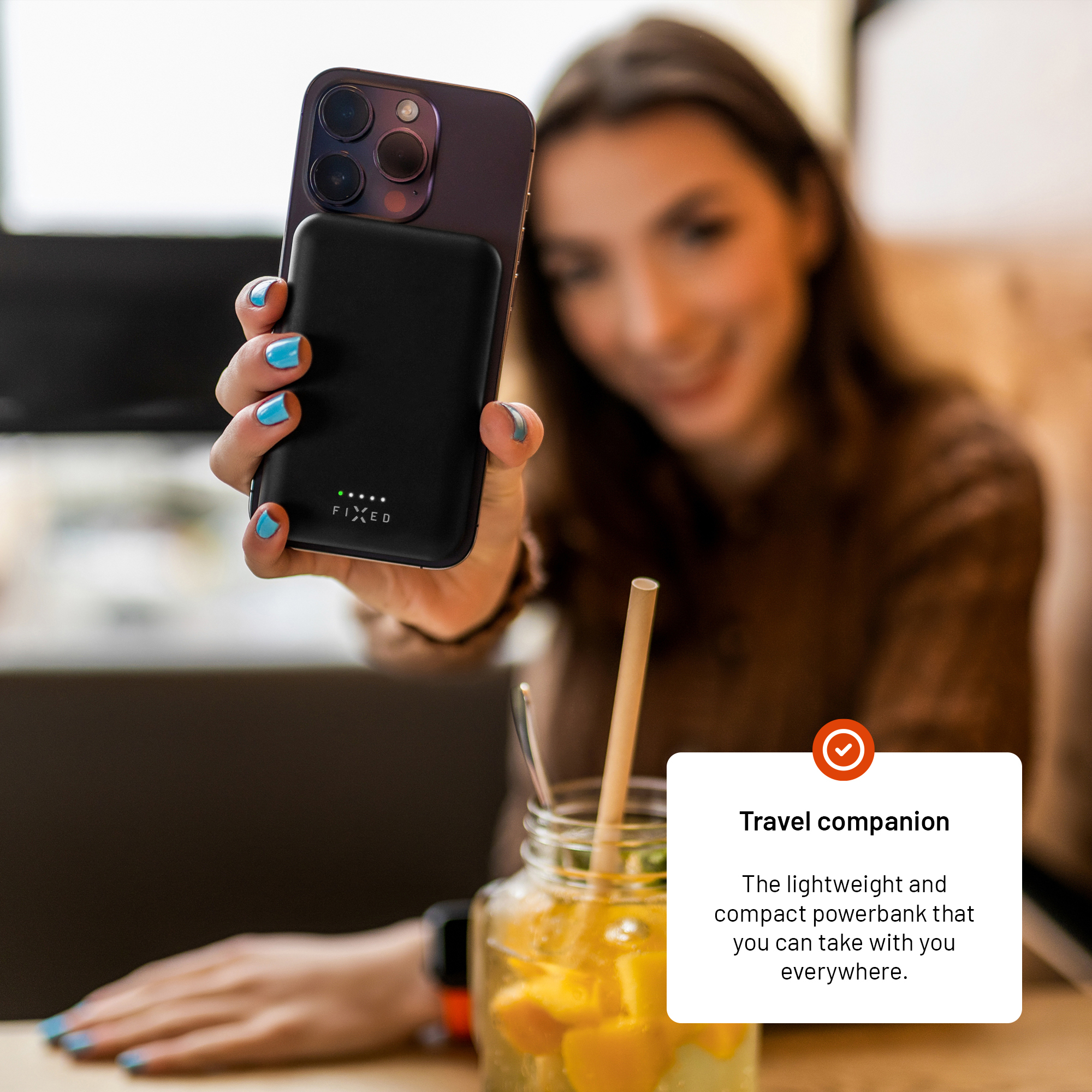 Eine Frau hält ein Smartphone mit einer schwarzen Powerbank auf der Rückseite in einem Café.
