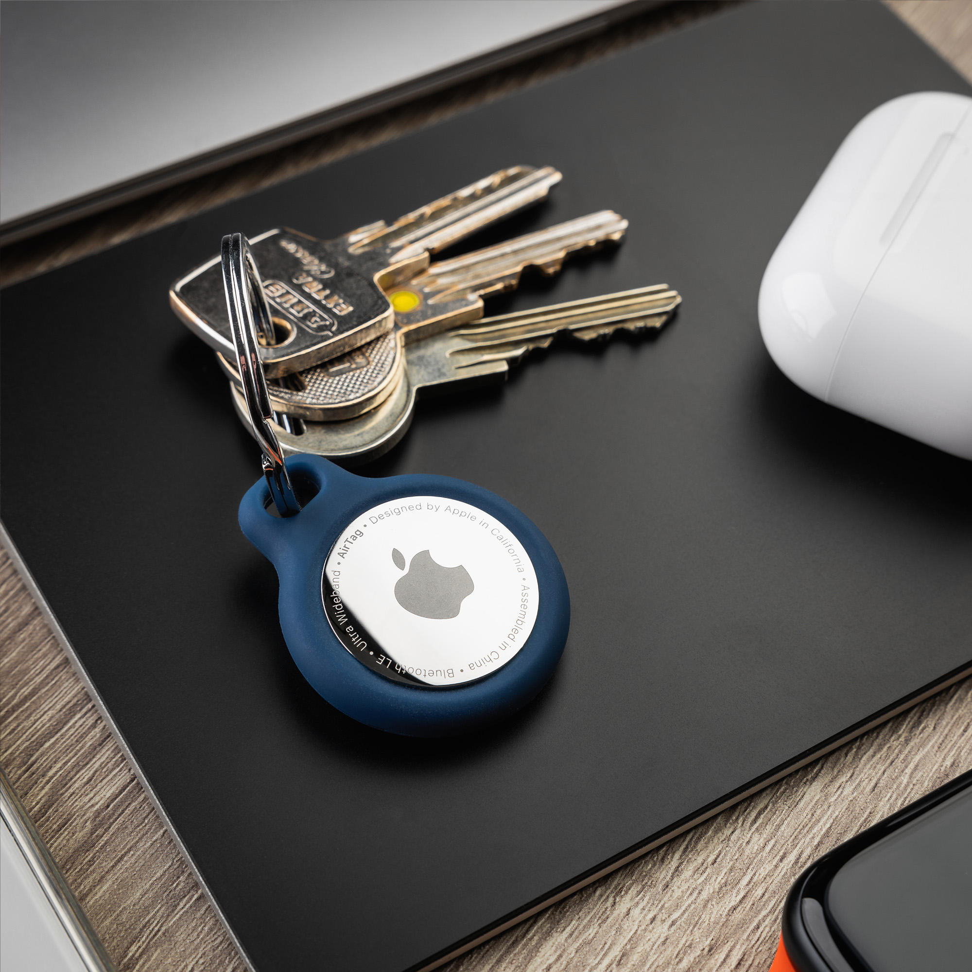 Ein blauer Apple AirTag mit Schlüsseln und Kopfhörern auf einem schwarzen Pad.