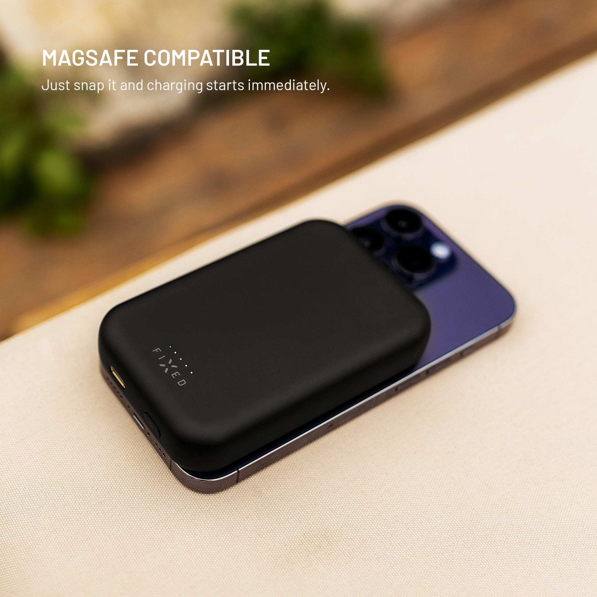 Schwarze Magsafe-Powerbank lädt ein violettes Smartphone auf einem Tisch.