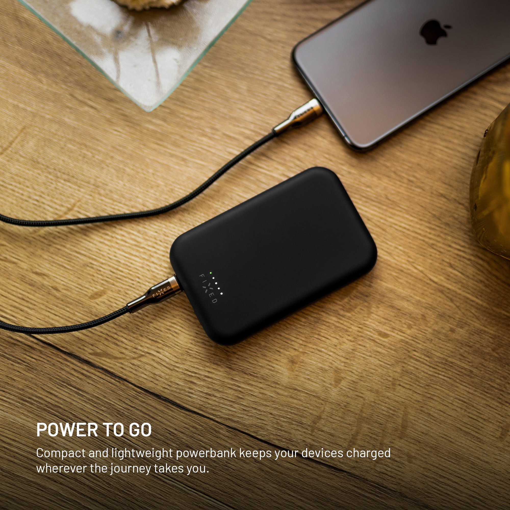 Eine schwarze Powerbank lädt ein Smartphone auf einem Holztisch.