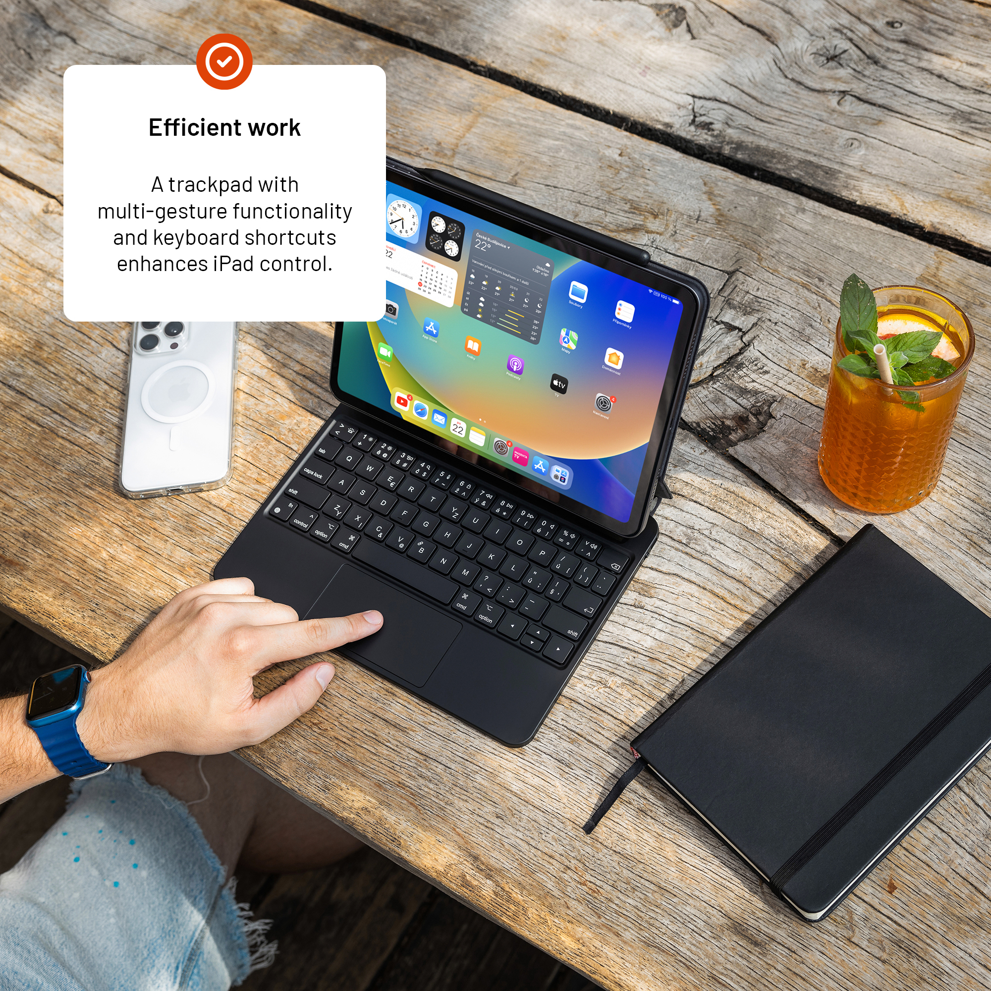 Ein iPad mit Tastaturhülle, Trackpad, Smartphone, Getränk und Notizbuch auf einem Holztisch.