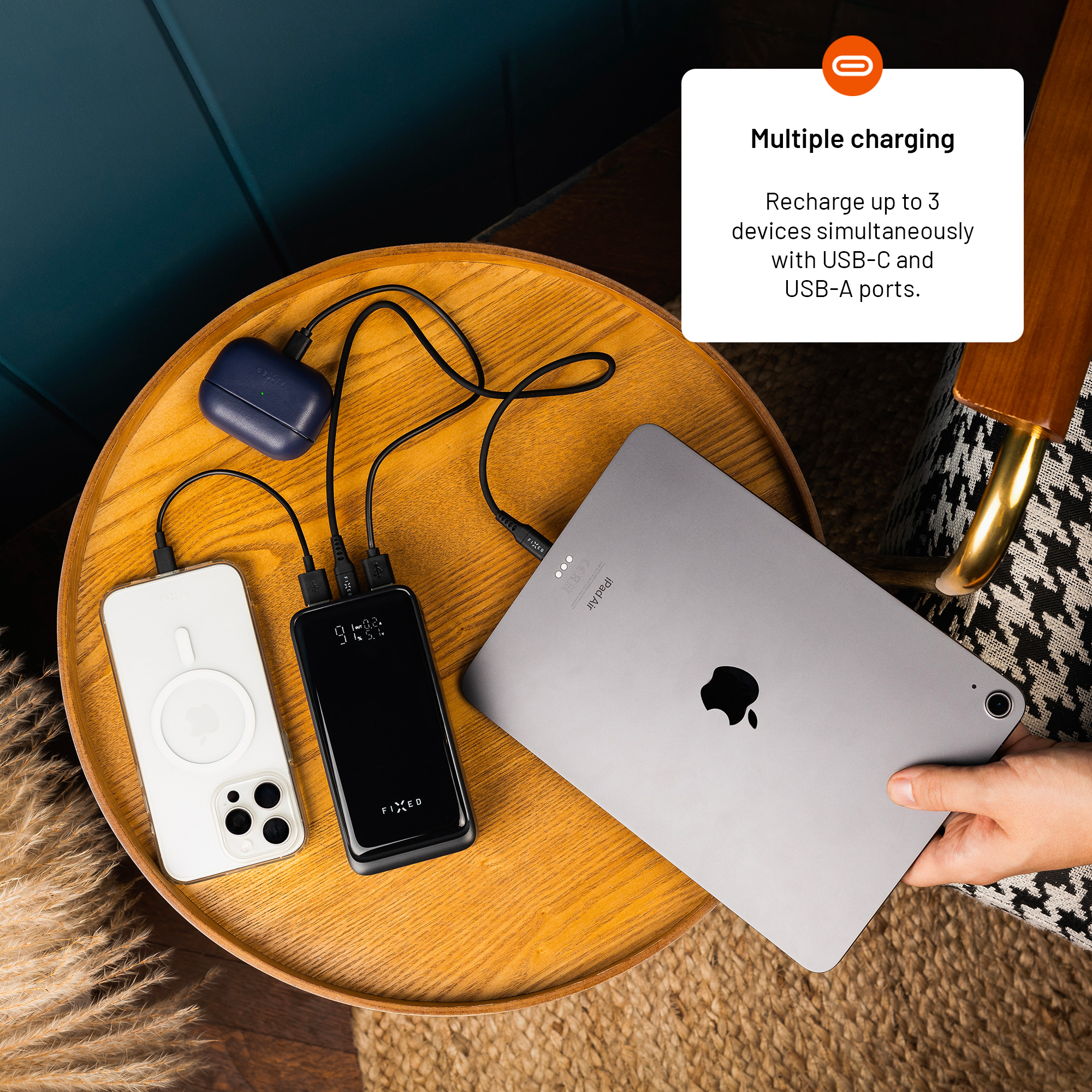 Eine Powerbank auf einem Holztisch lädt gleichzeitig ein Handy, Kopfhörer und ein iPad.