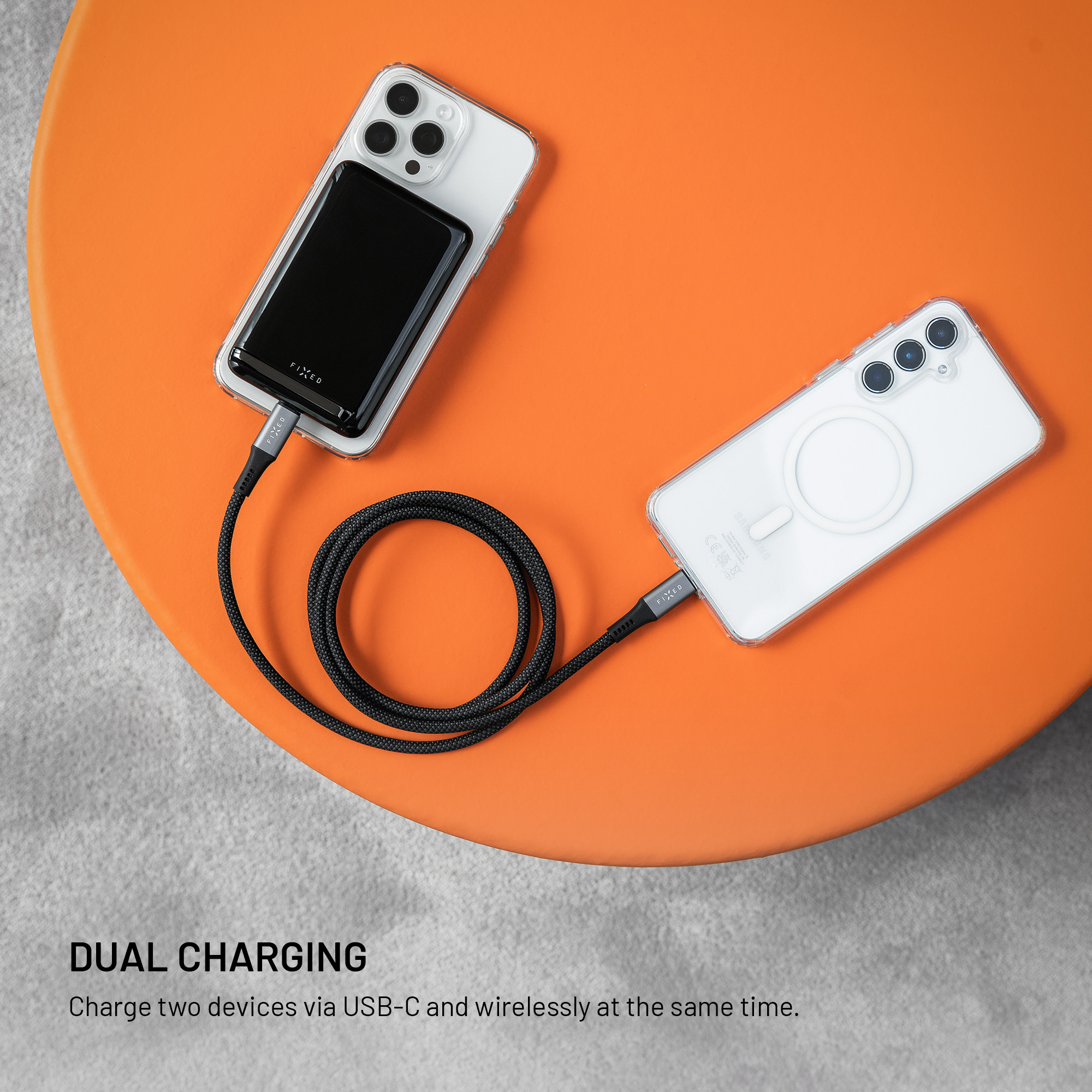 Zwei Smartphones liegen auf einem runden orangen Tisch und werden mit einem schwarzen USB-C-Kabel verbunden und geladen.