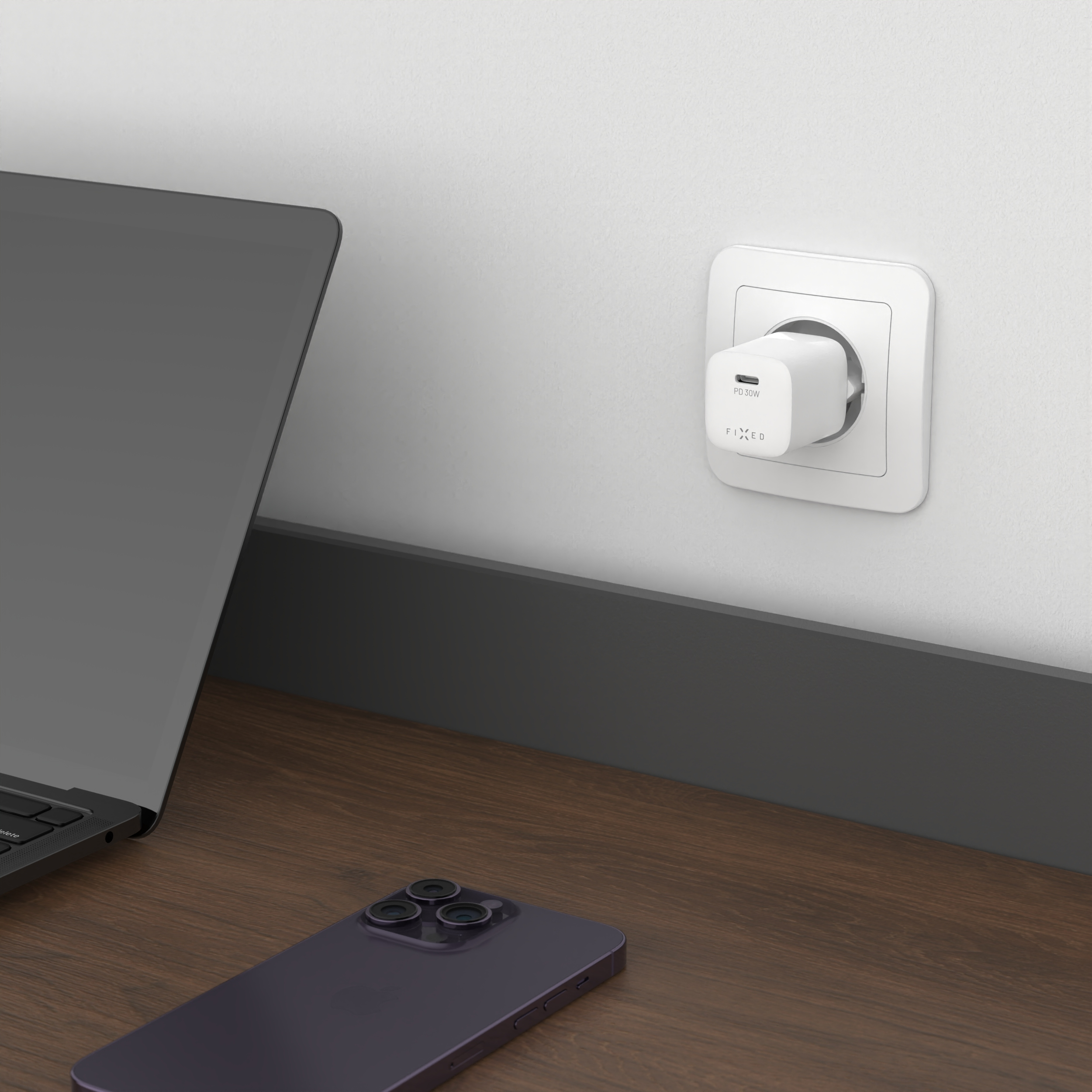 Ein weißes PD 30W Ladegerät steckt in der Wand, ein Laptop und ein dunkles Smartphone liegen auf dem Tisch.