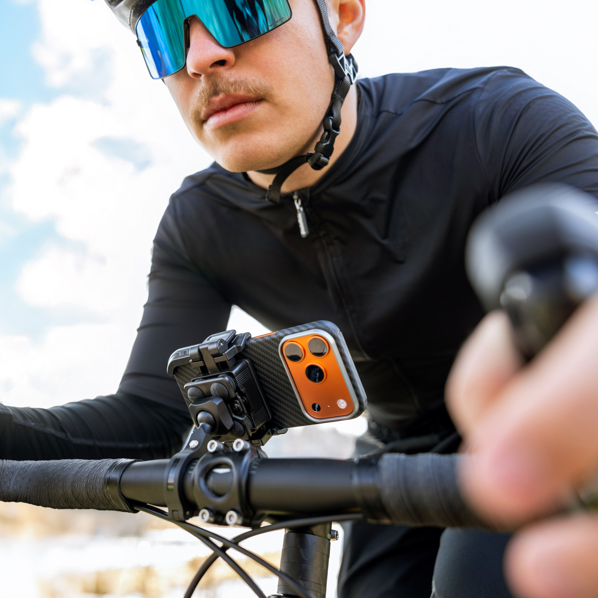 Ein Radfahrer mit verspiegelten Sonnenbrillen und schwarzem Trikot, ein Smartphone am Lenker montiert.