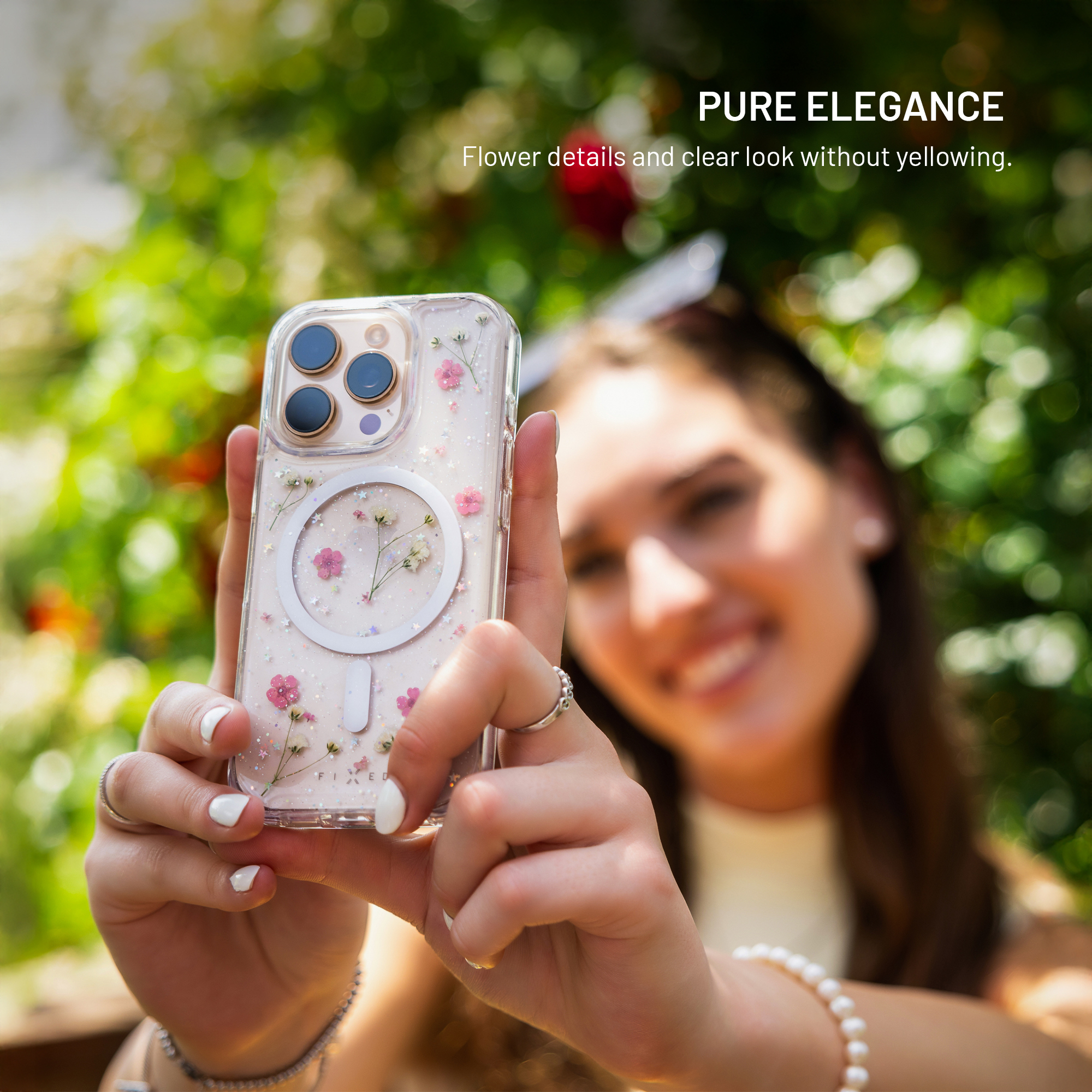 Eine Frau hält eine klare Handyhülle mit kleinen Blumenmustern im Sonnenlicht. Text oben: PURE ELEGANCE.