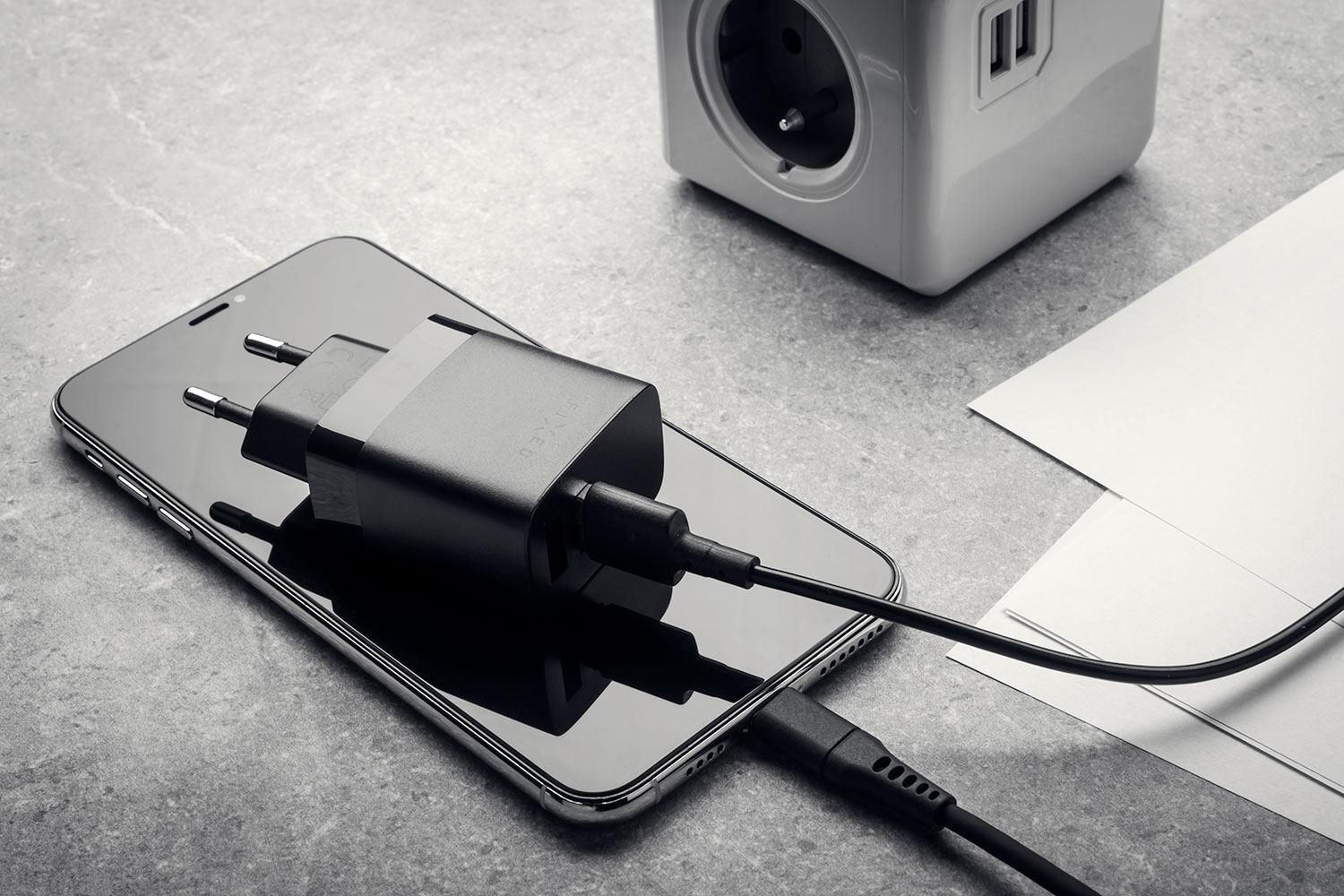 Ein schwarzes Smartphone liegt auf einer grauen Oberfläche und wird mit einem schwarzen Ladegerät aufgeladen.