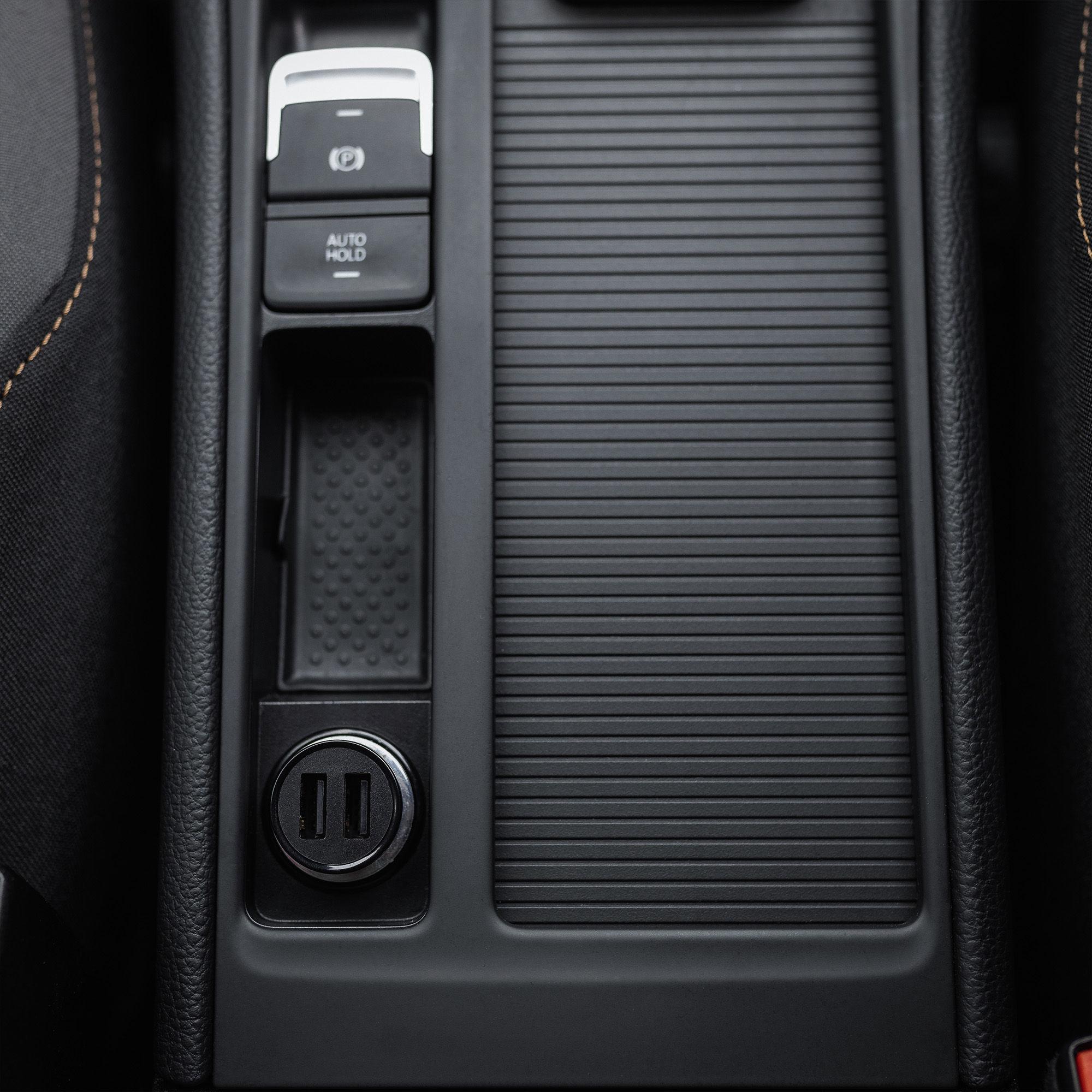 Schwarze Autokonsole mit elektrischer Handbremse, kleiner Ablage und zwei USB-Anschlüssen.