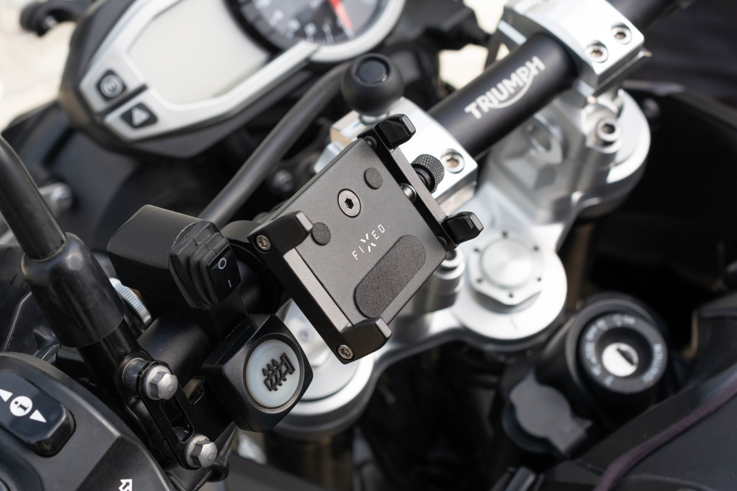 Nahaufnahme einer schwarzen FIXED-Smartphone-Halterung am Triumph-Motorradlenker mit Bedienelementen.