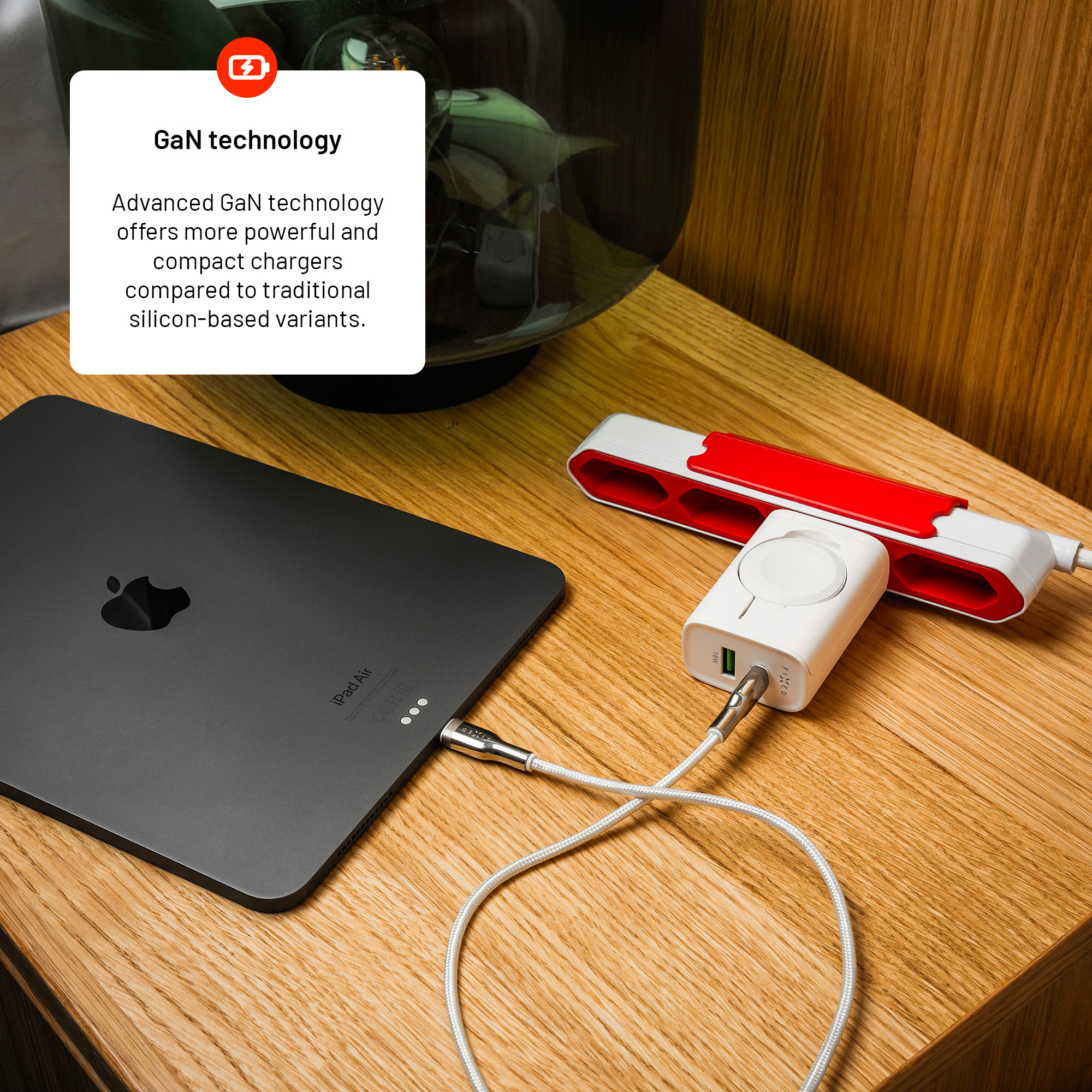 Ein schwarzes iPad Air lädt an einem weißen Ladegerät mit Kabel auf einer Holzoberfläche.