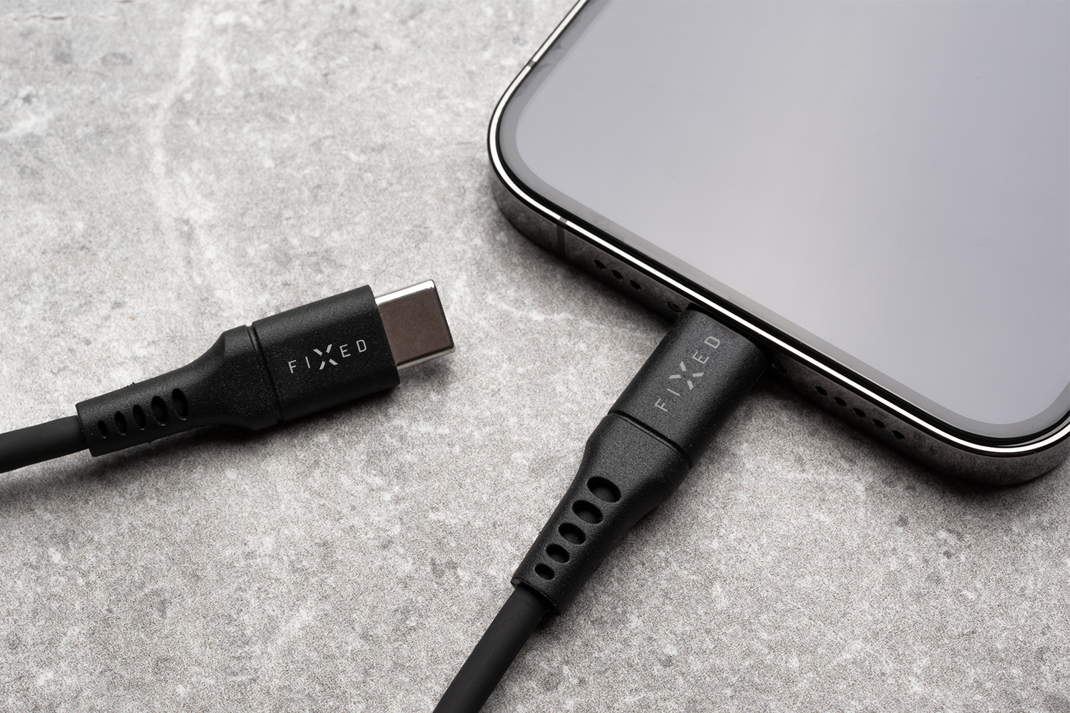Ein schwarzes USB-C-Kabel mit FIXED-Branding steckt in einem Smartphone, daneben ein weiteres Kabel auf grauem Grund.