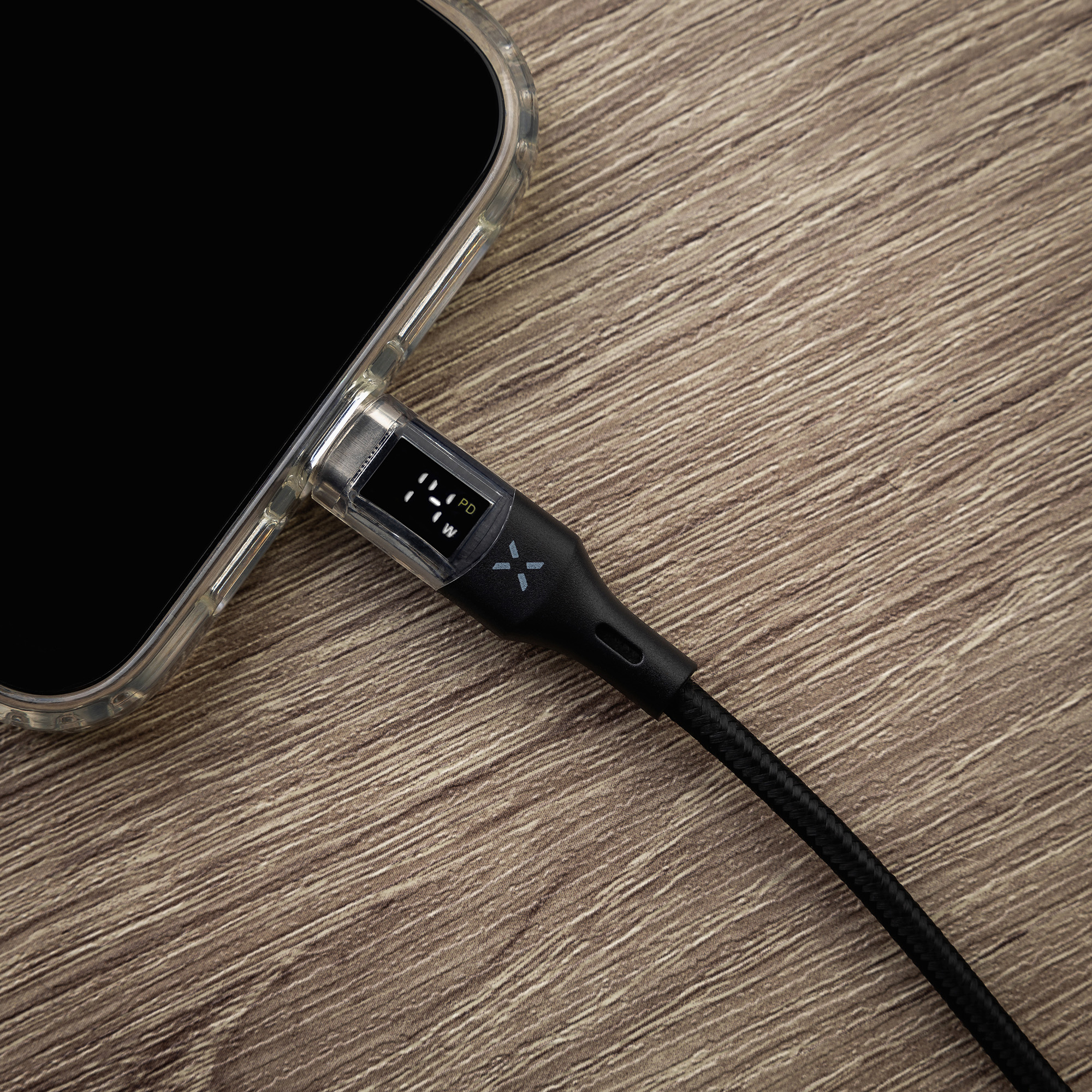 Ein Smartphone in Schutzhülle wird auf Holzoberfläche mit schwarzem USB-C-Kabel mit Display und Watt-Anzeige geladen.