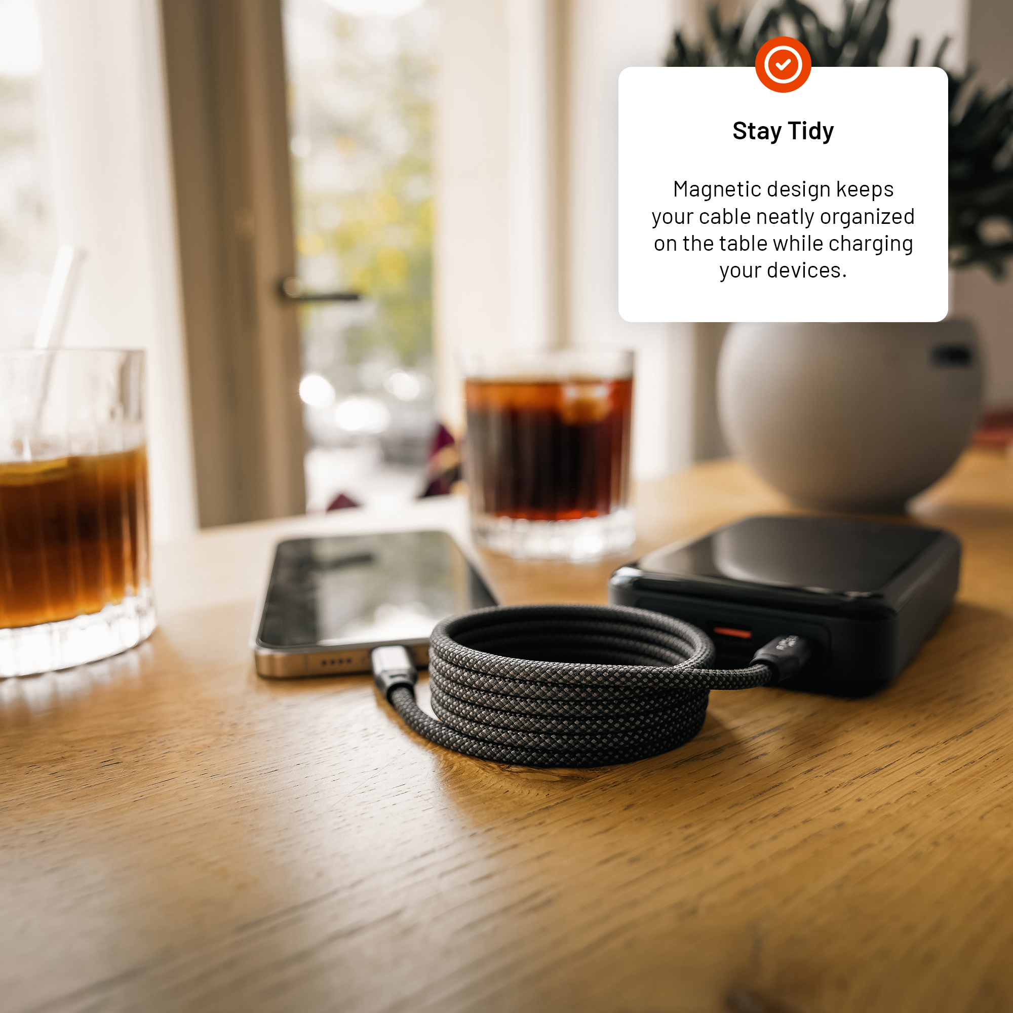 Gerolltes geflochtenes Kabel auf einem Holztisch verbindet ein Telefon mit einer Powerbank, mit Textoverlay.