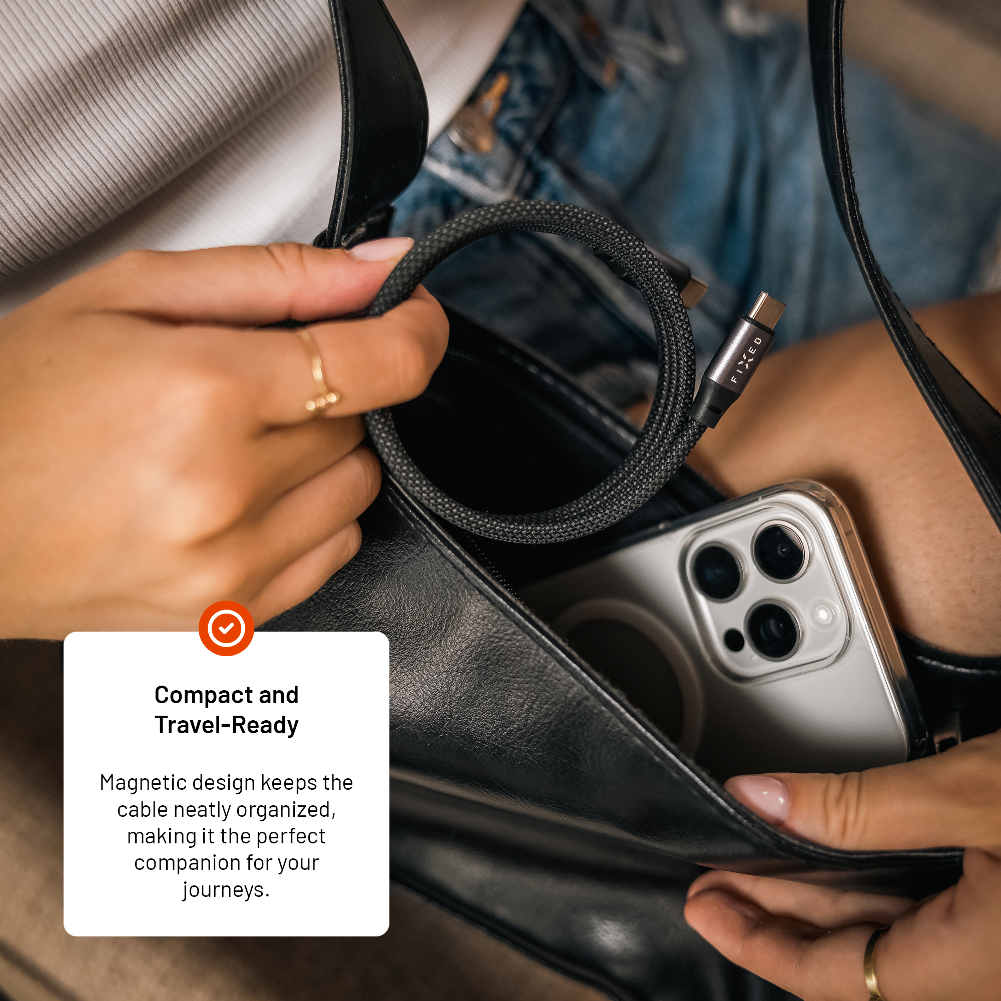 Eine Person hält ein gerolltes, schwarzes Kabel in einer Hand und eine Handtasche mit Smartphone.