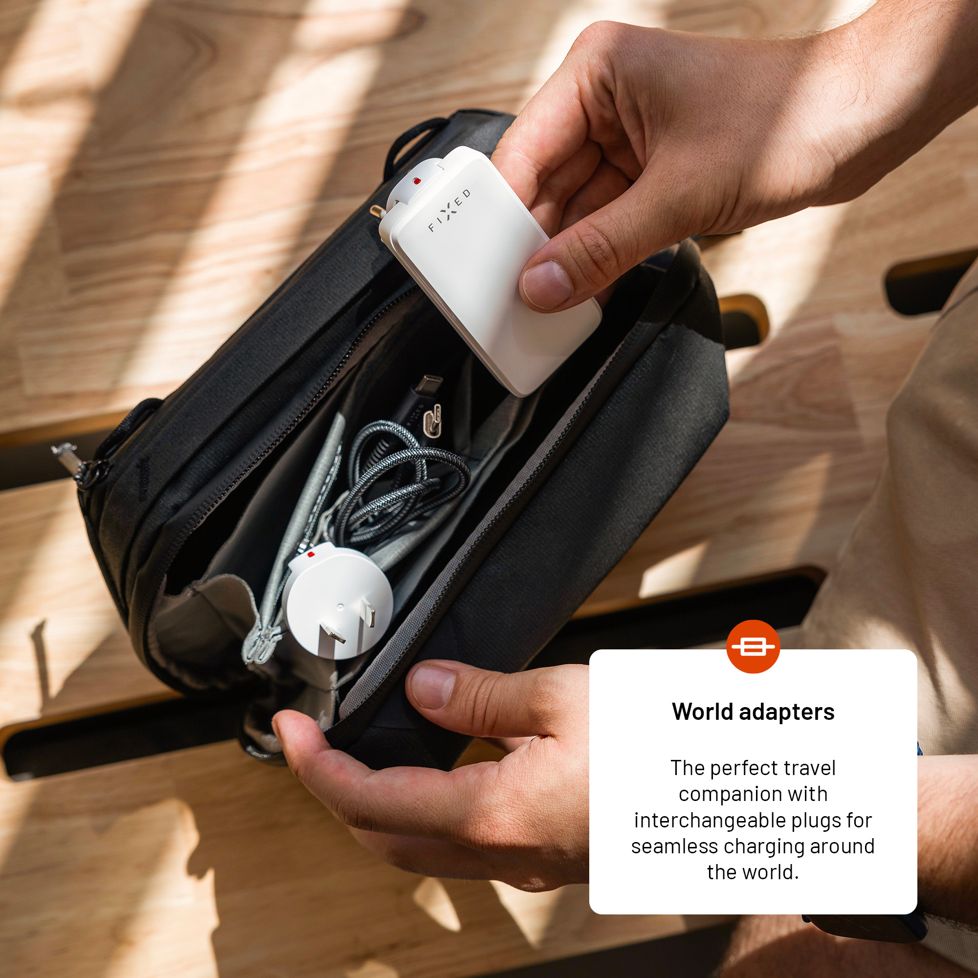 Person packt einen weißen Reiseadapter in eine schwarze Tasche mit Kabeln.
