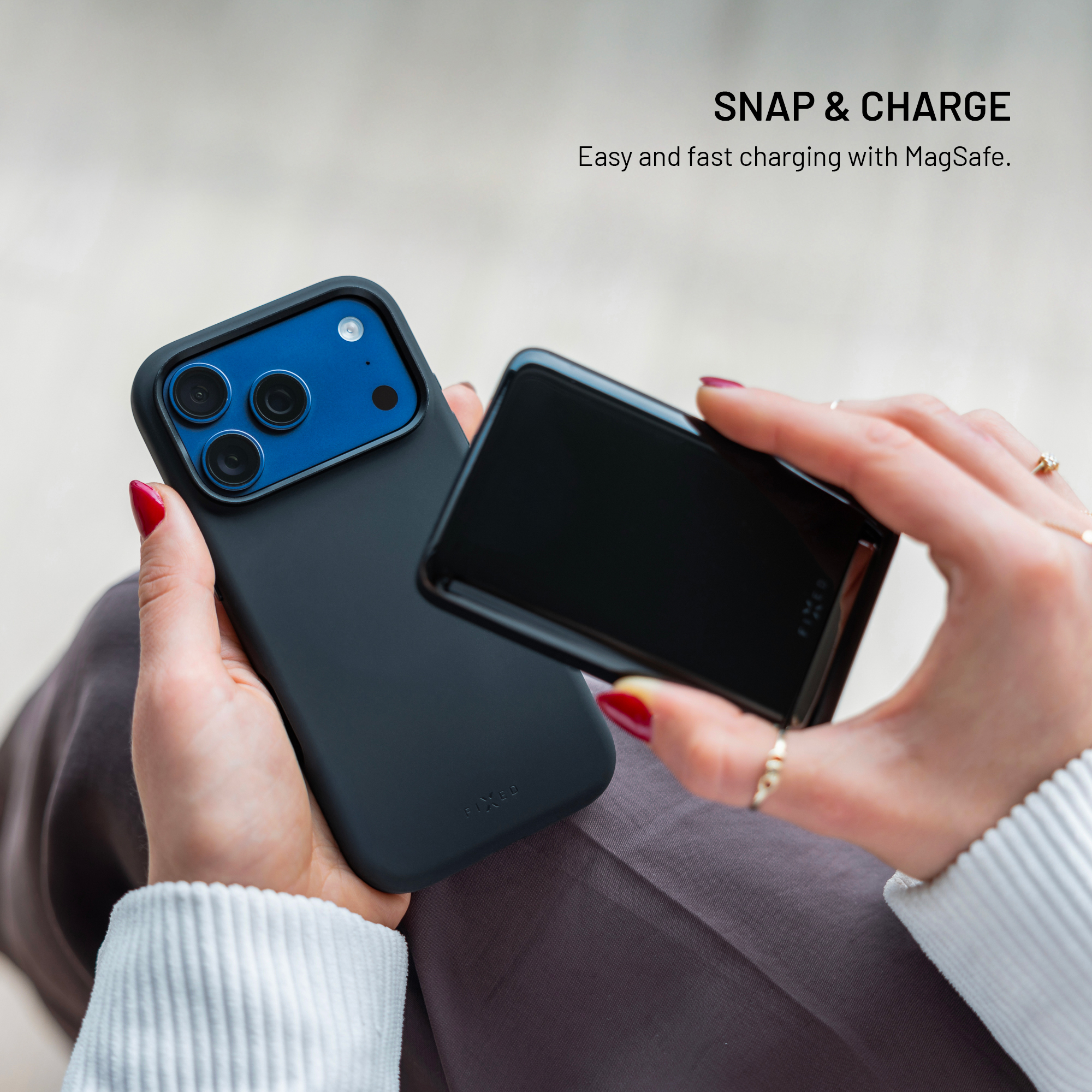 Hände halten ein schwarzes Smartphone mit blauer Kamera und eine MagSafe-Powerbank darüber.