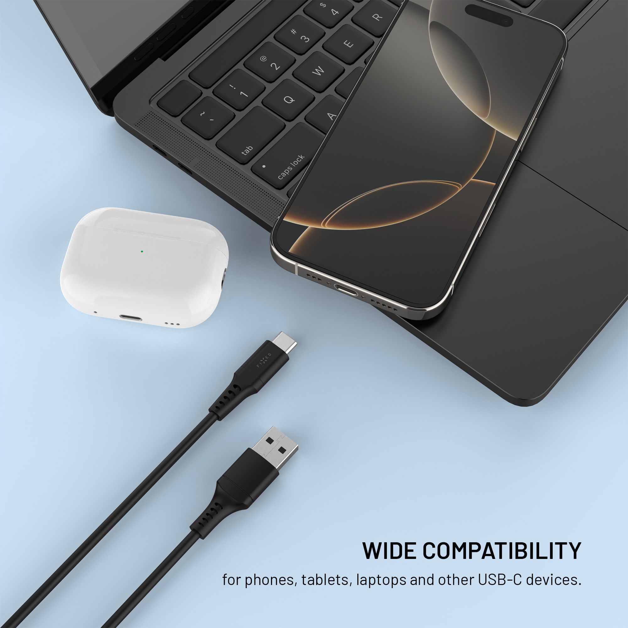 Uno smartphone, auricolari wireless e cavi USB-C su una superficie blu accanto a un laptop.