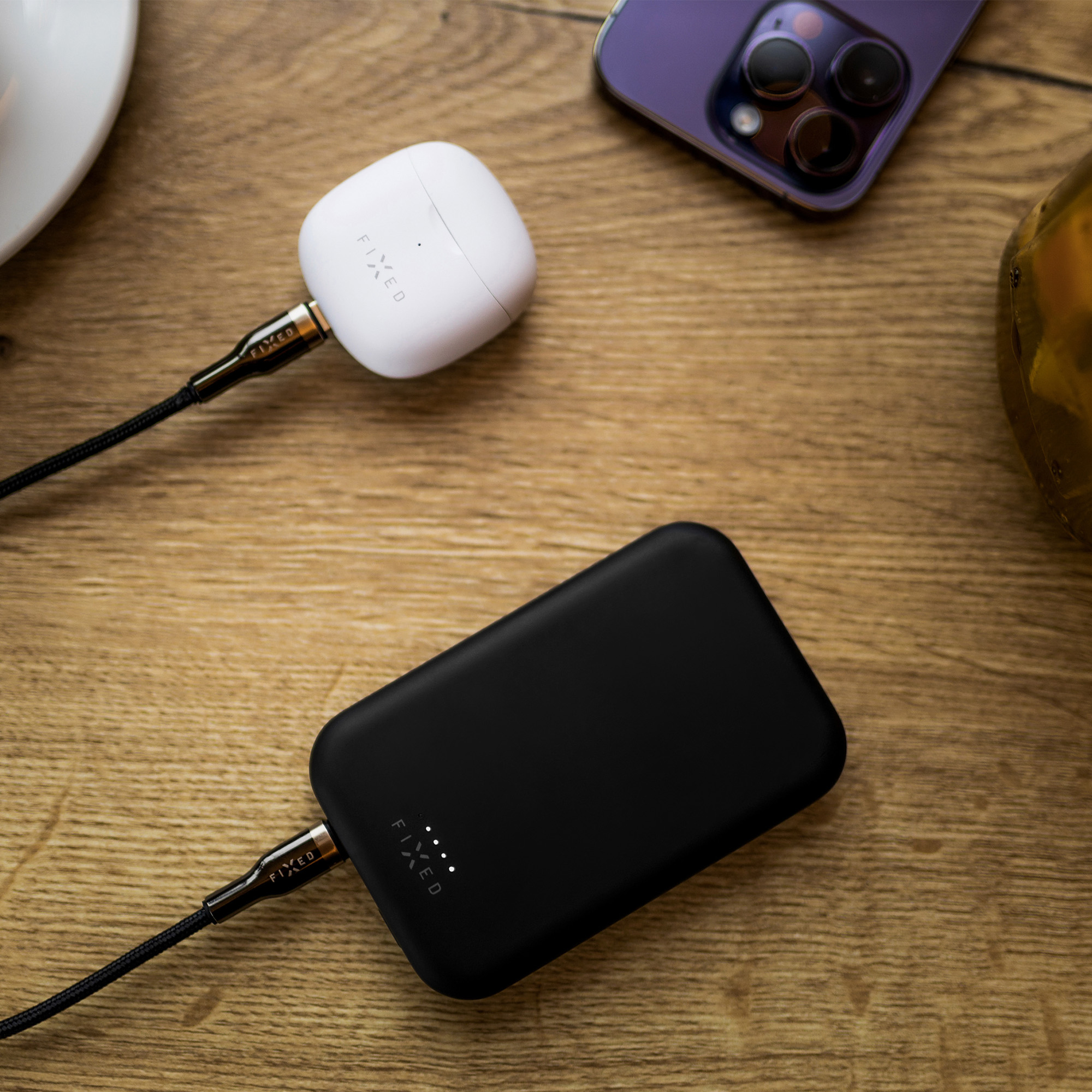 Eine Powerbank, ein Kopfhörer-Ladecase und ein Smartphone liegen auf einer Holztischplatte.