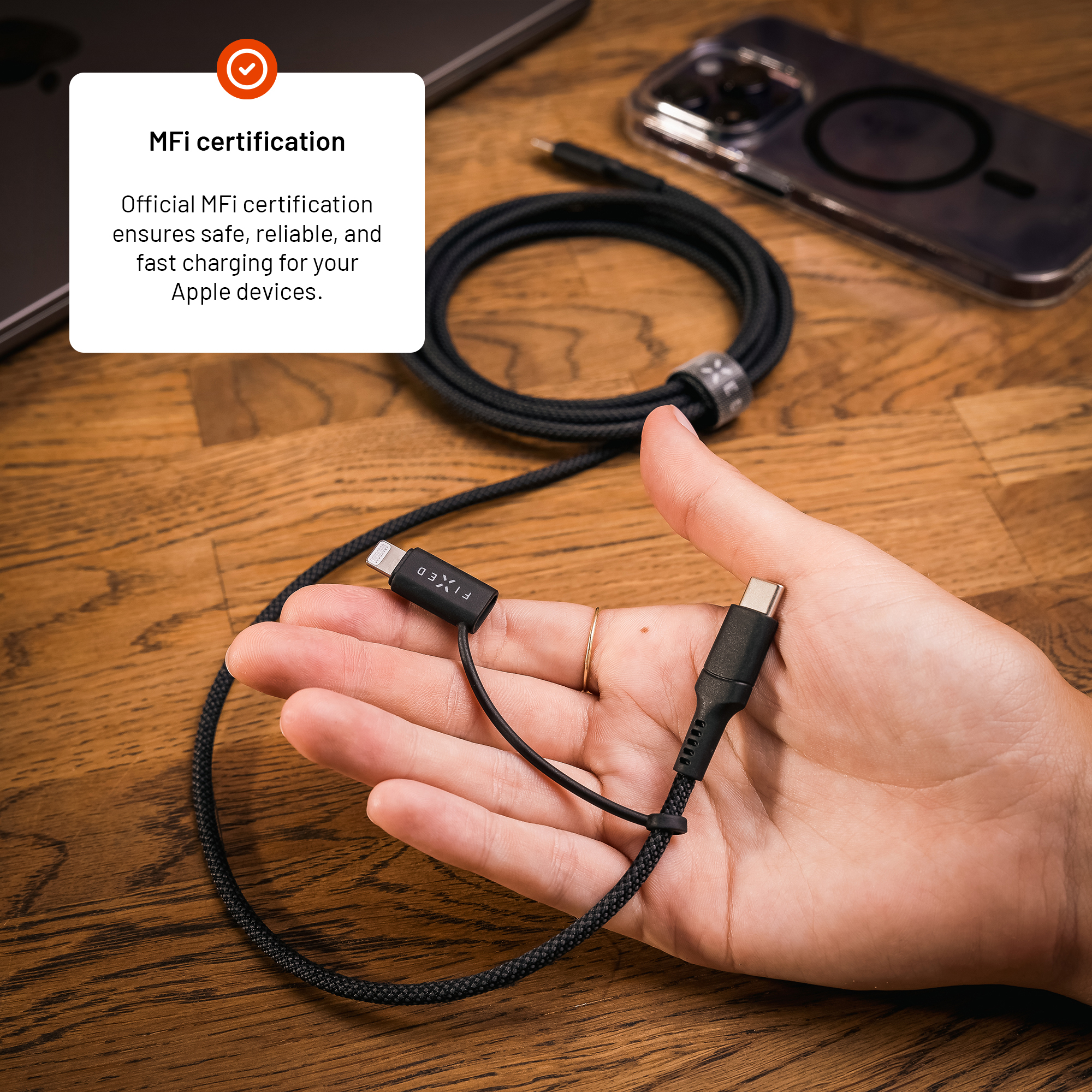 Hand hält ein geflochtenes schwarzes Ladekabel mit USB-C- und Lightning-Anschlüssen auf Holz.