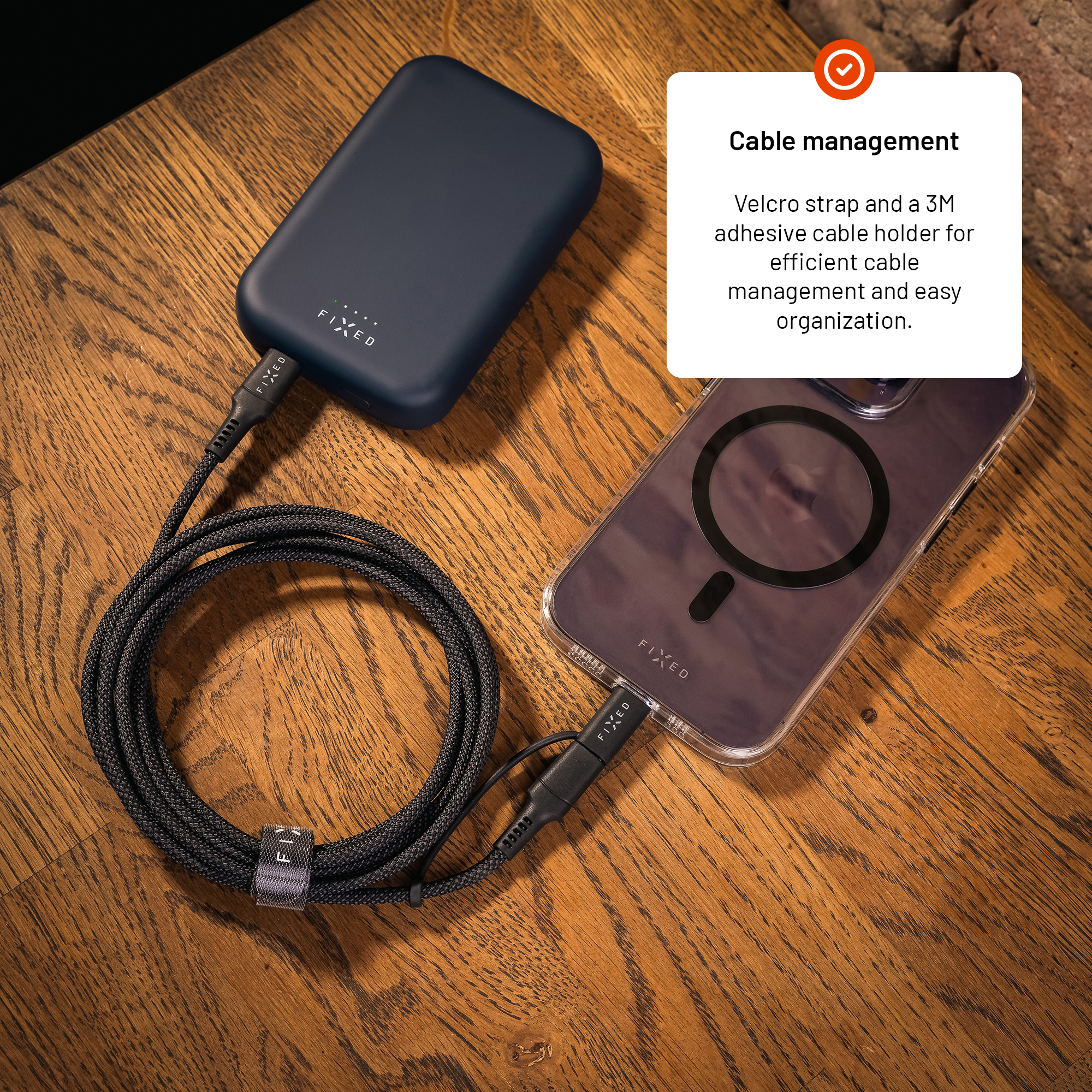Eine dunkelblaue Powerbank und ein Smartphone mit Schutzhülle liegen auf Holz und sind mit einem Kabel verbunden.