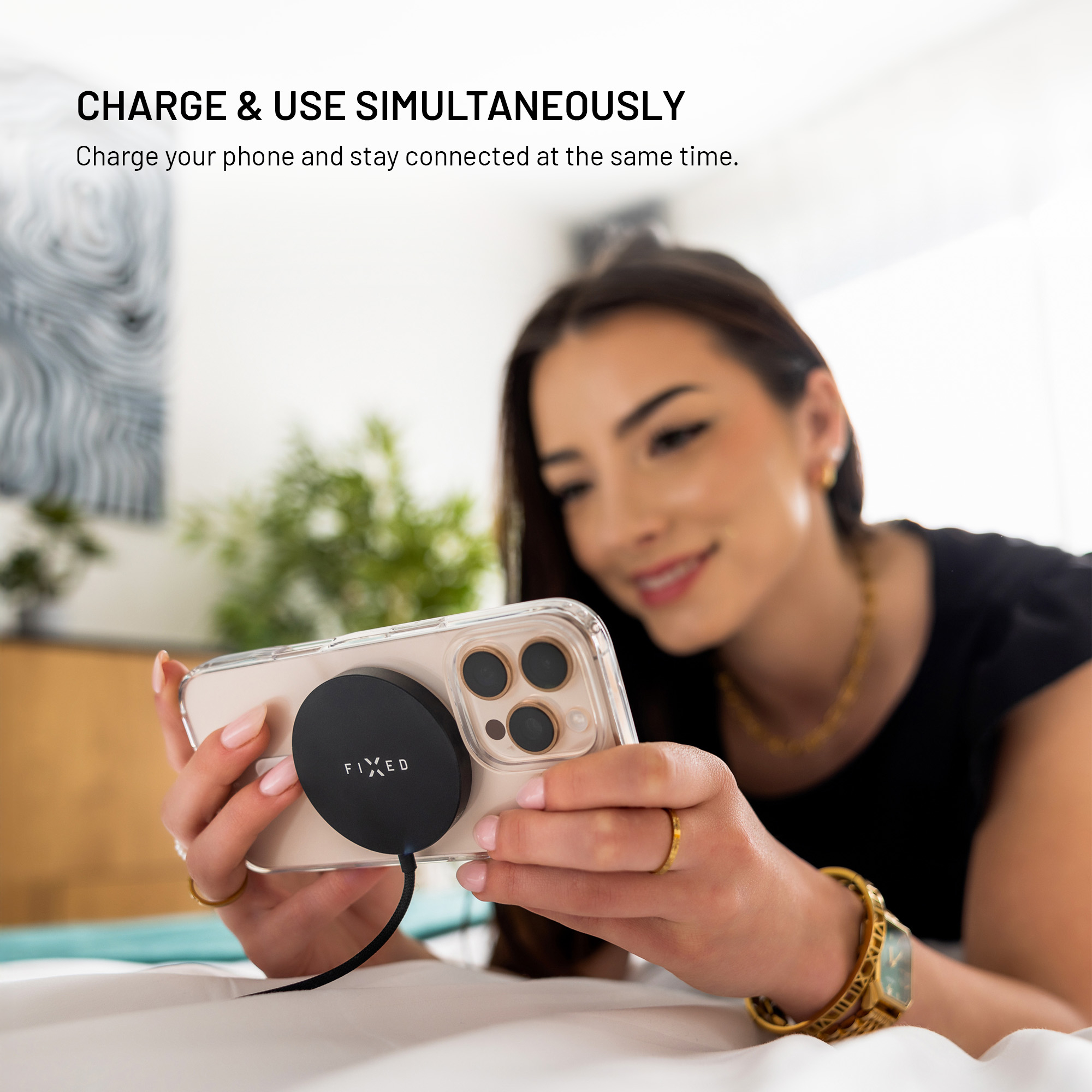 Eine lächelnde Frau hält ein Smartphone mit schwarzem, rundem Magnetladegerät auf der Rückseite.